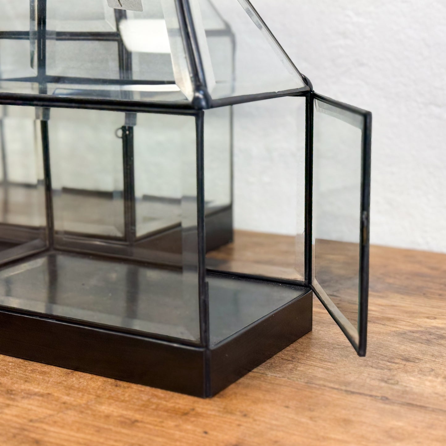 Glass display case with black metal frame on a wooden surface