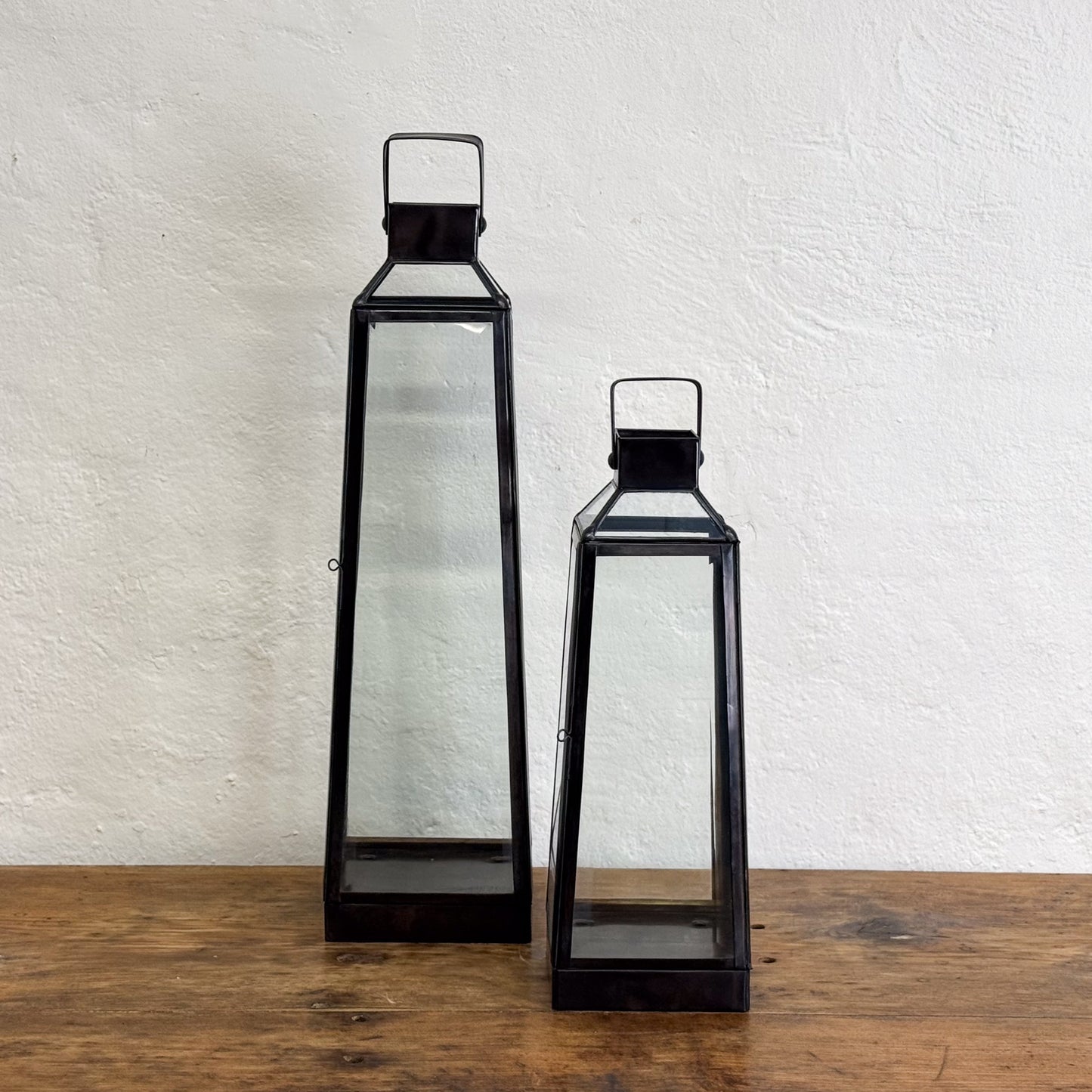 Two black lanterns on a wooden surface with a white textured wall background