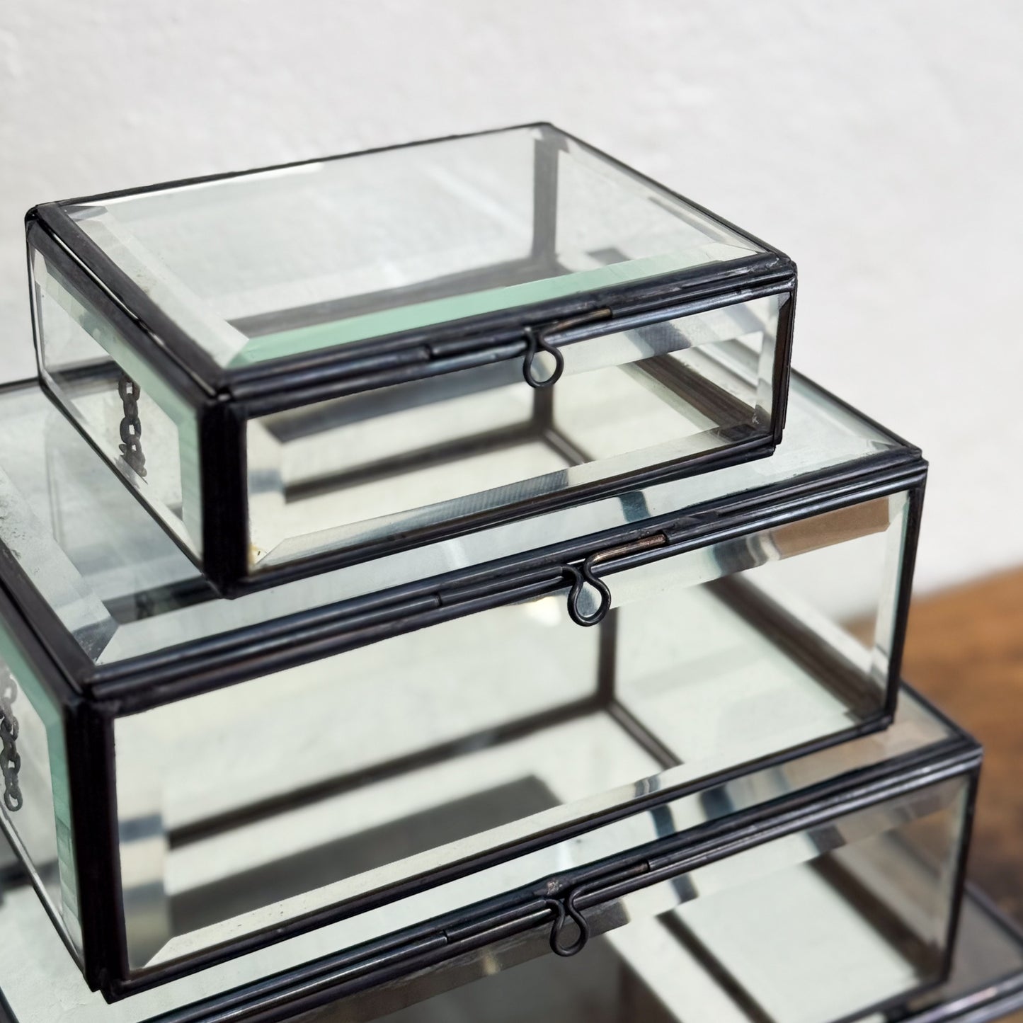 Stack of glass jewelry boxes with black metal accents on a reflective surface.