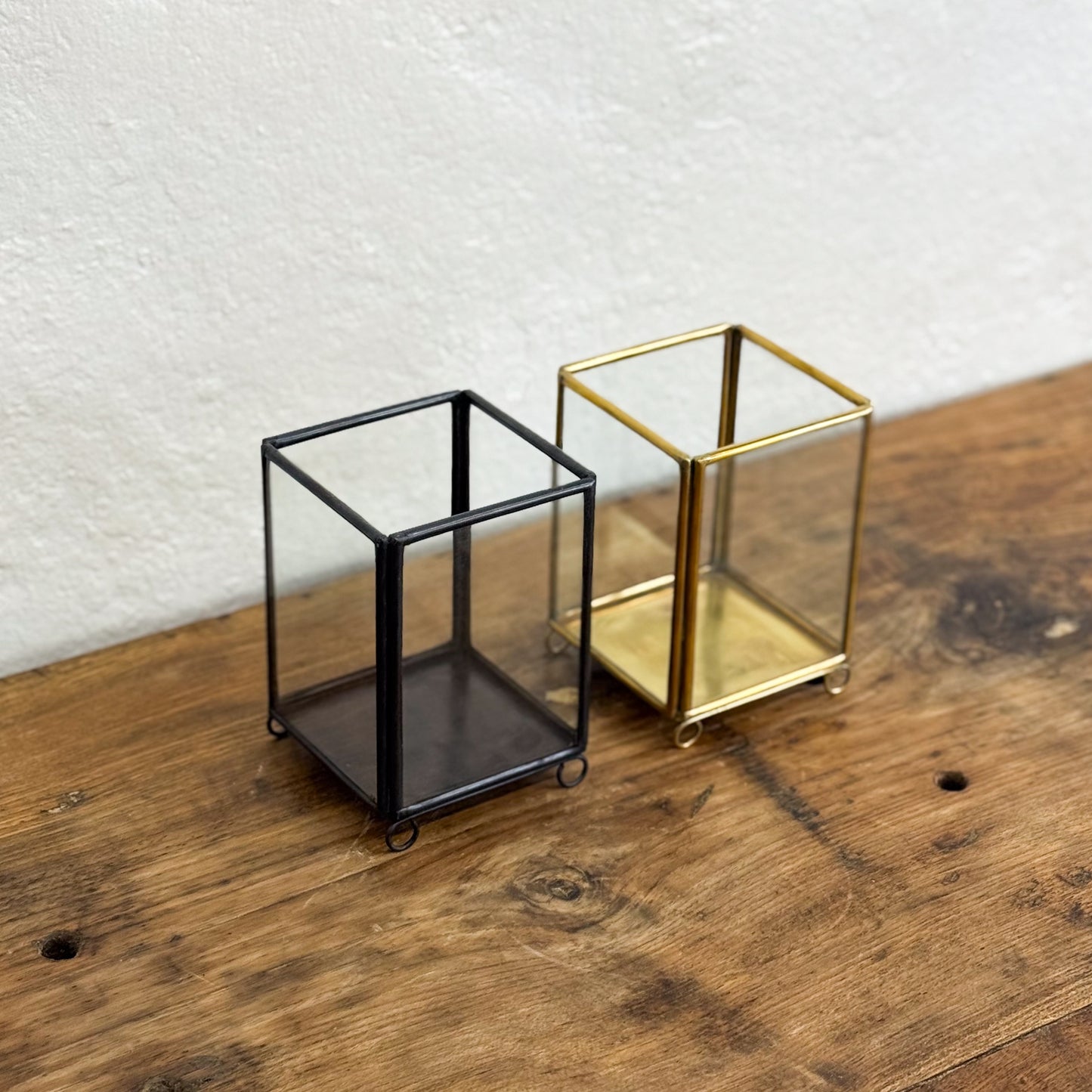 Two glass cubes, one black and one gold, on a wooden surface with a white textured wall background.