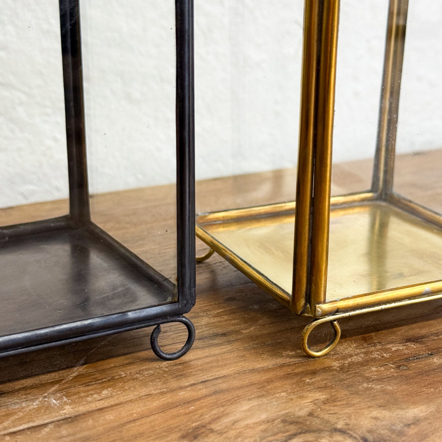 Two decorative glass boxes, one black and one gold, on a wooden surface with a white textured wall background.