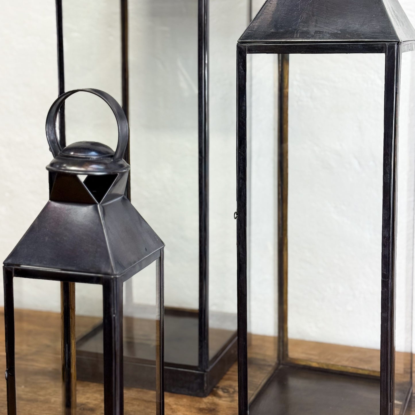 Two black metal lanterns on a wooden surface with a white wall background