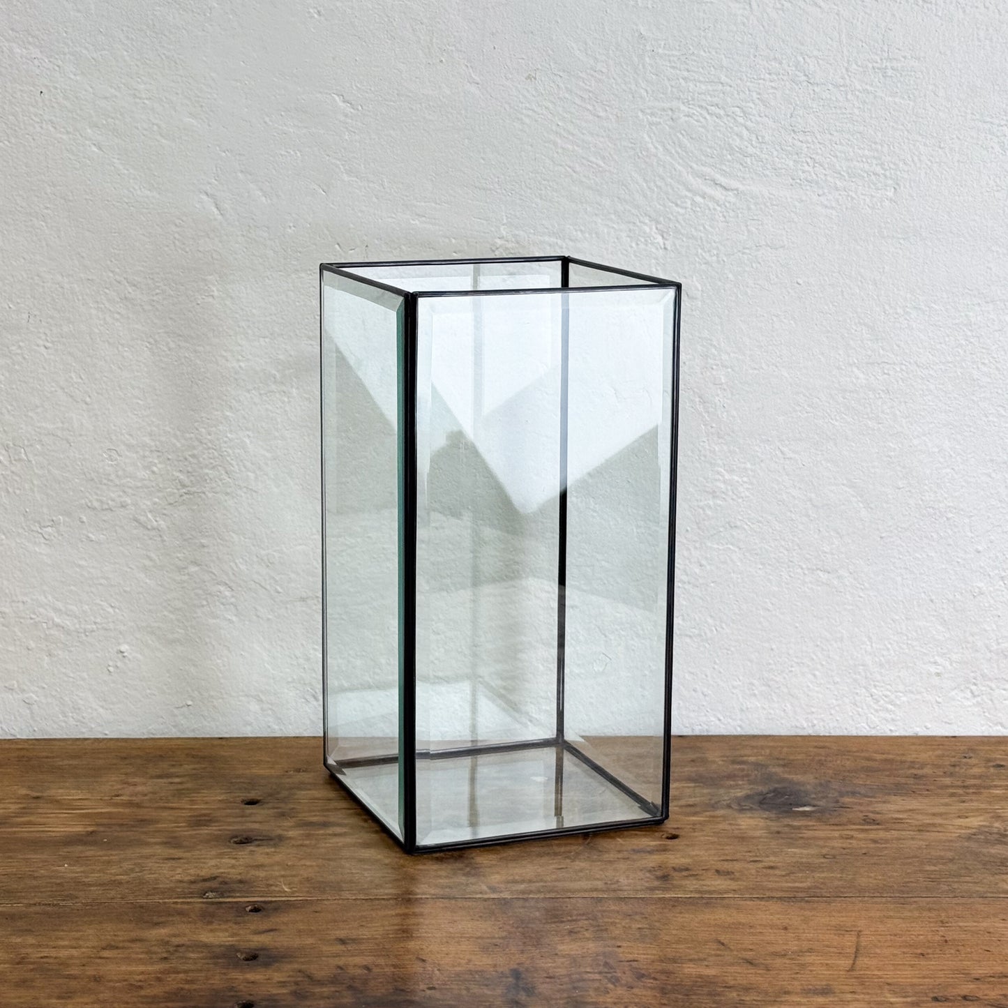 Clear glass cube with black frame on a wooden surface and white wall background