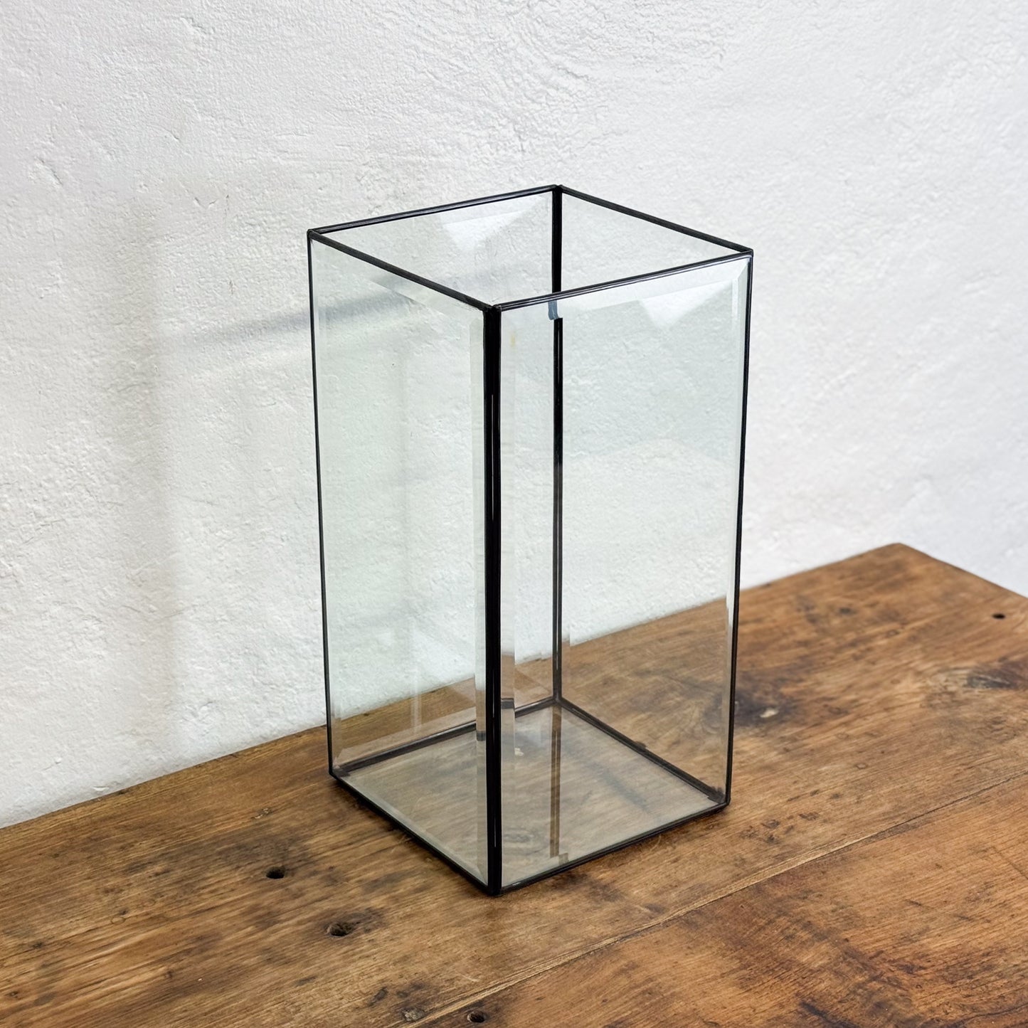 Clear glass square vase on a wooden surface with a white textured wall background