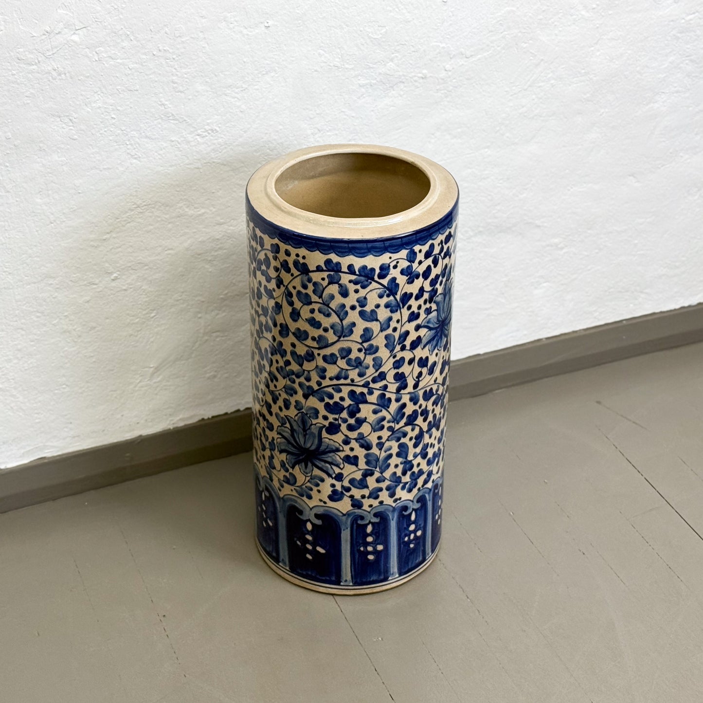 Cylindrical ceramic vase with blue floral patterns against a white wall.