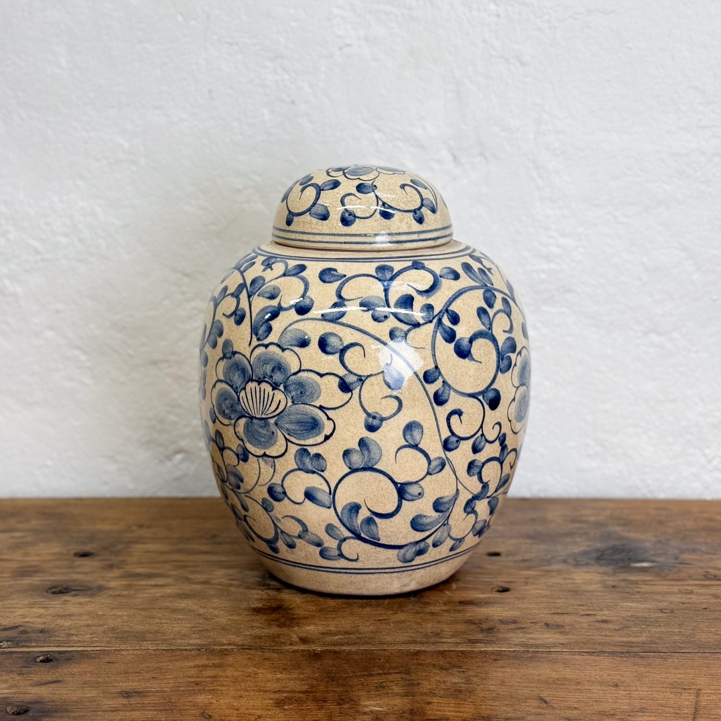 Ceramic jar with blue floral patterns on a wooden surface and white textured wall background