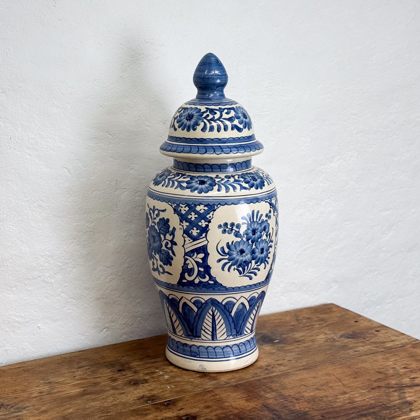 Blue and white ceramic jar with lid on a wooden surface against a white wall