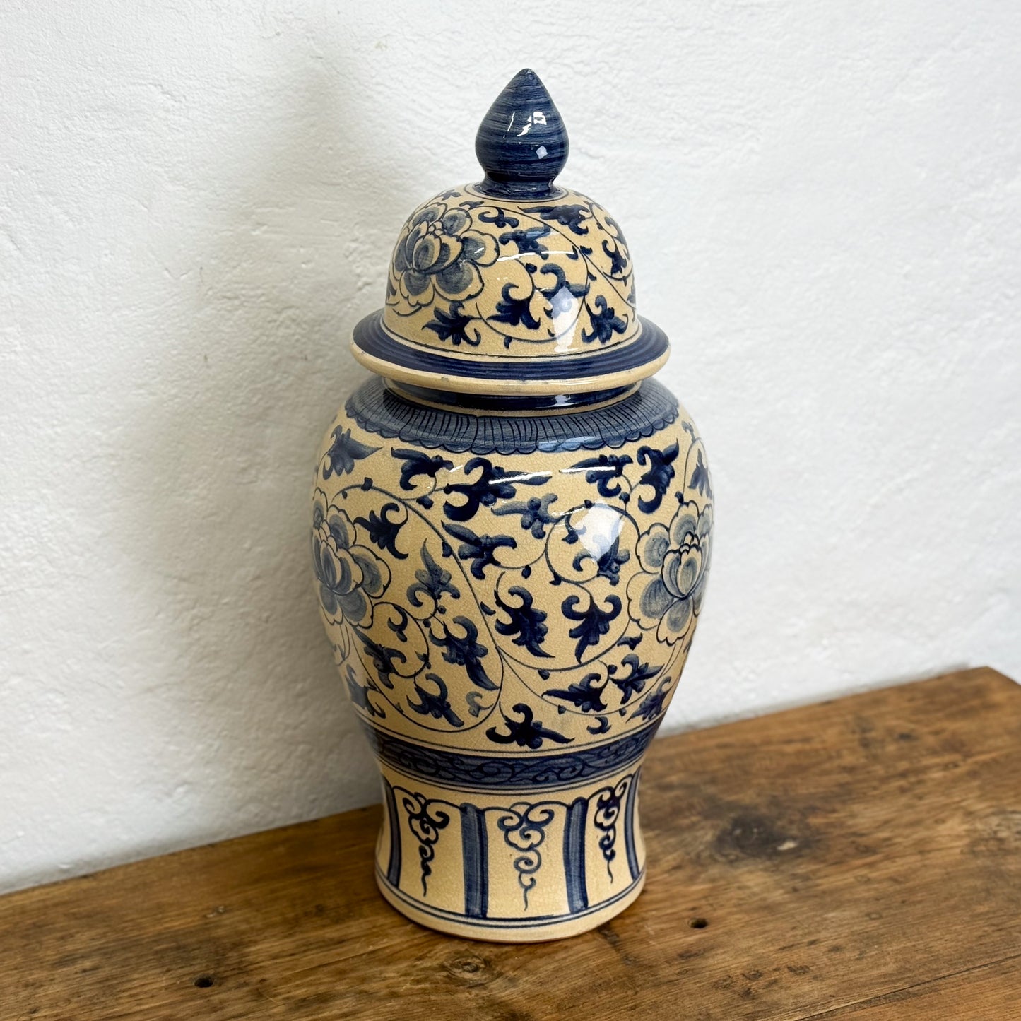 Ceramic jar with blue floral patterns on a wooden surface against a white wall