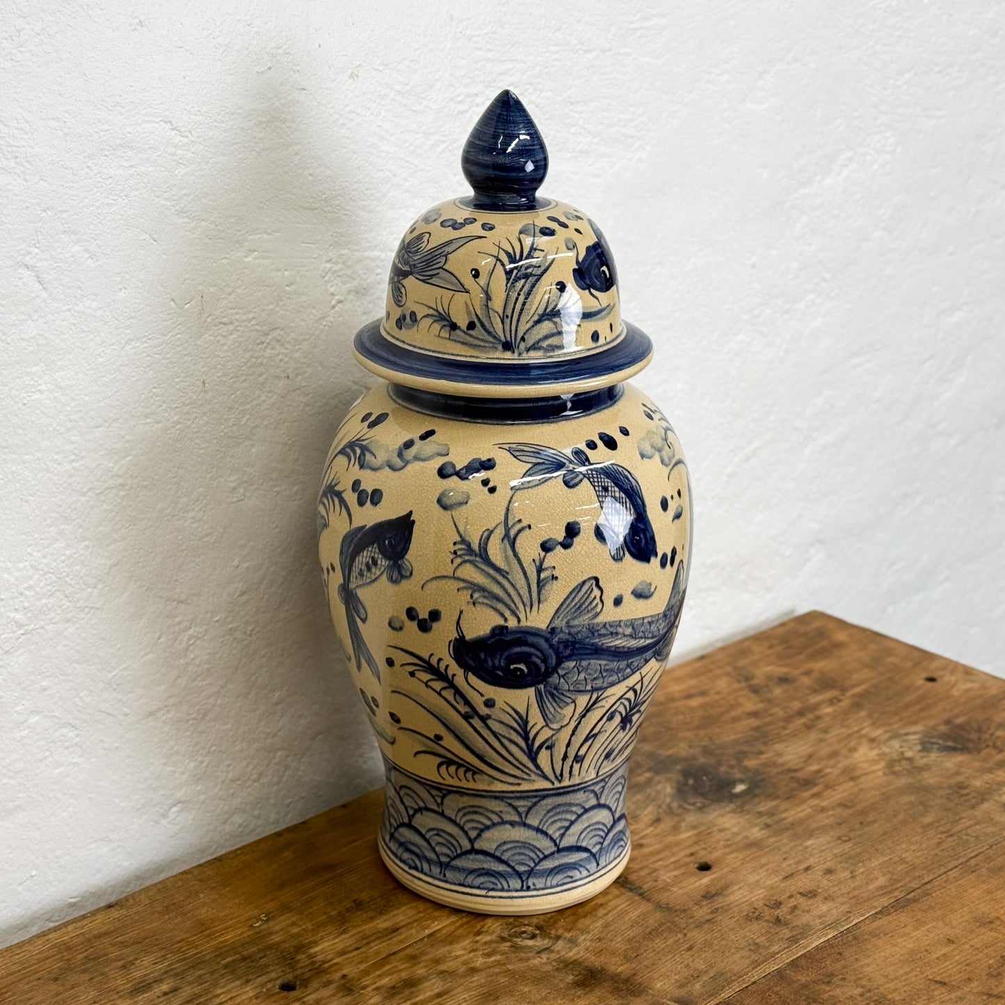 Ceramic jar with blue floral and fish design on a wooden surface against a white wall