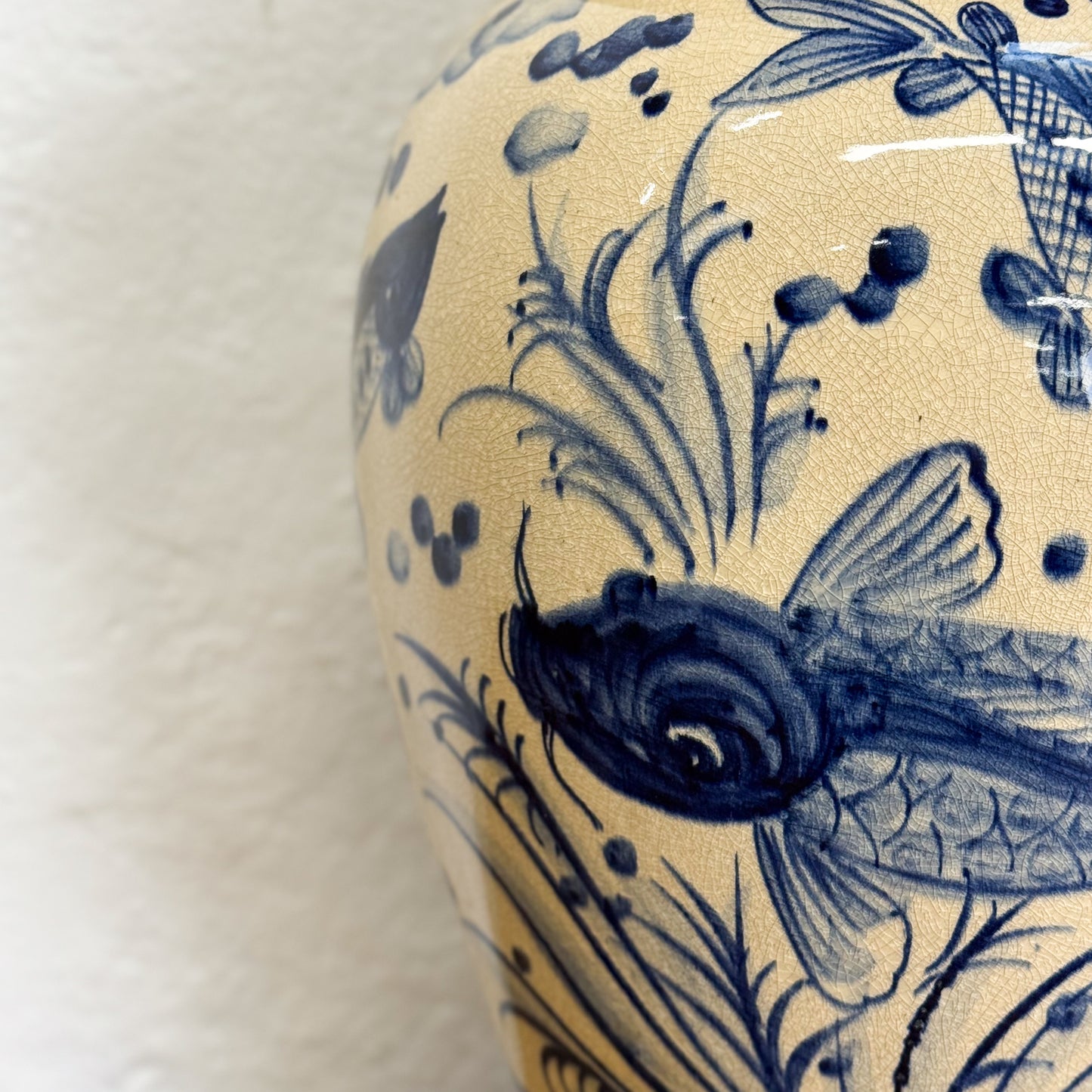 Ceramic vase with blue fish and plant designs on a beige background
