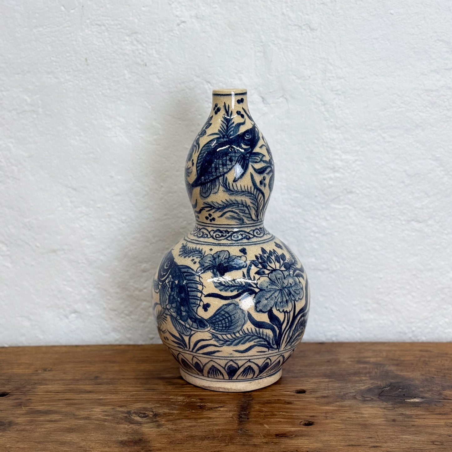 Blue and white ceramic vase with floral patterns on a wooden surface and white wall background