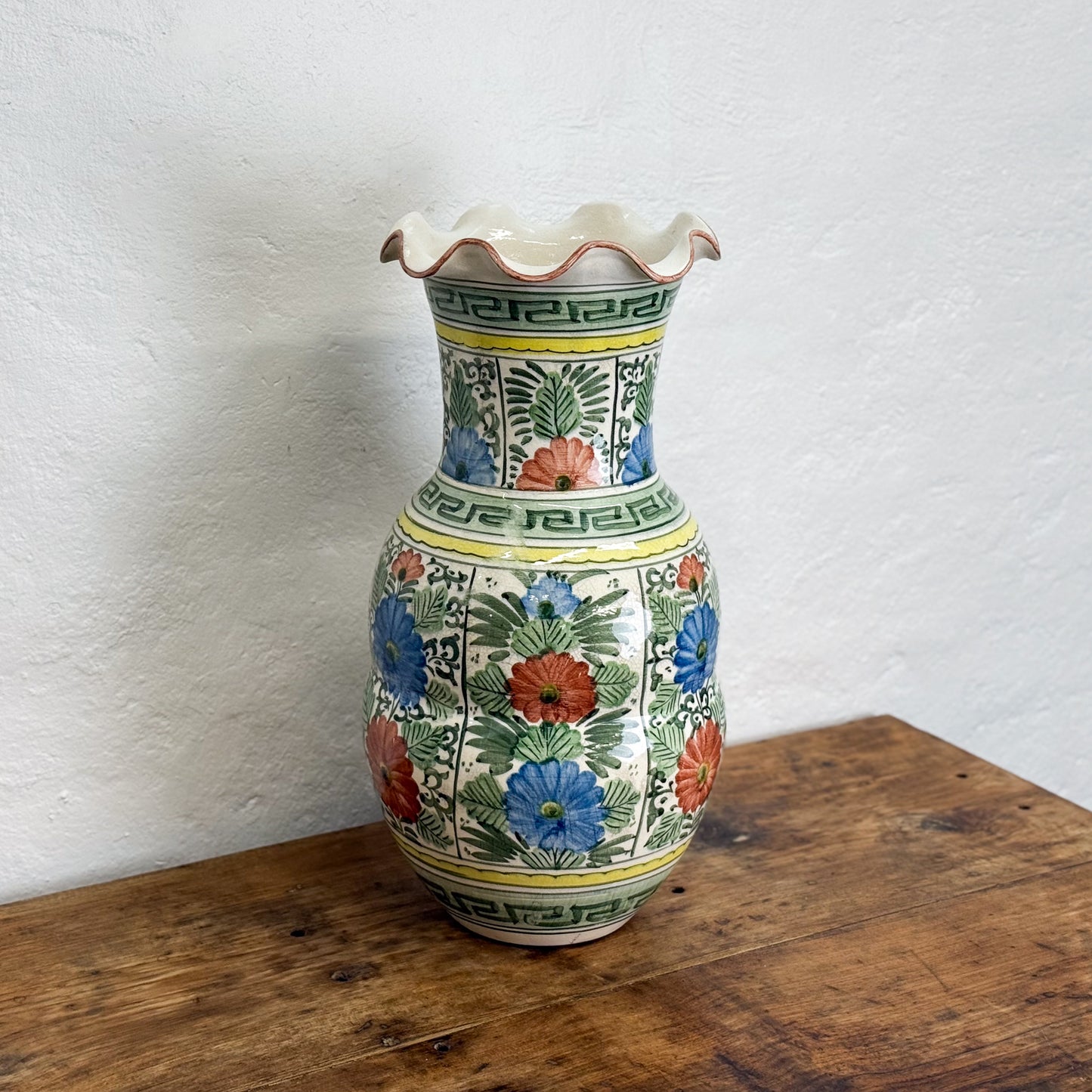 Decorative ceramic vase with floral patterns on a wooden surface against a white wall