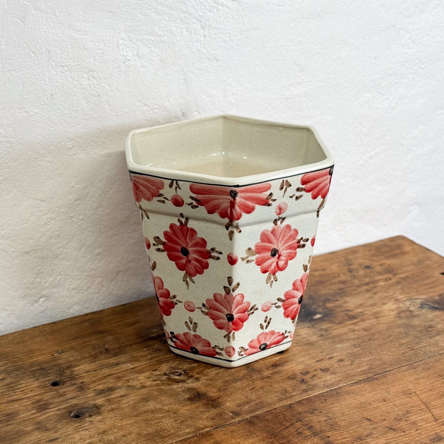 Decorative hexagonal pot with floral pattern on a wooden surface against a white wall