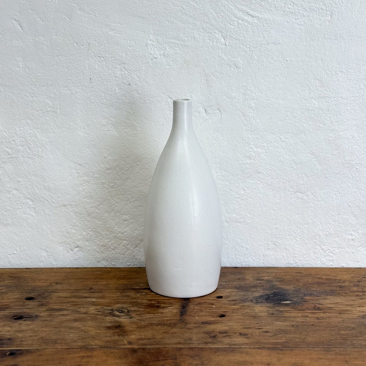 White ceramic bottle on a wooden surface with a white textured wall background