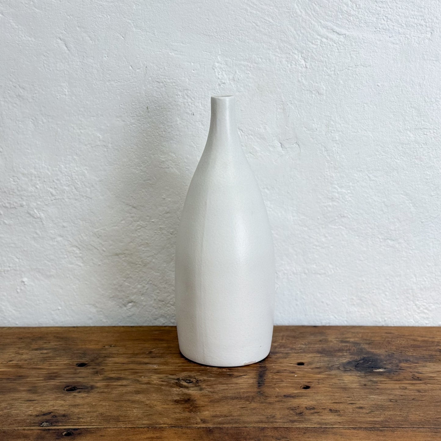 White ceramic bottle on a wooden surface with a white wall background