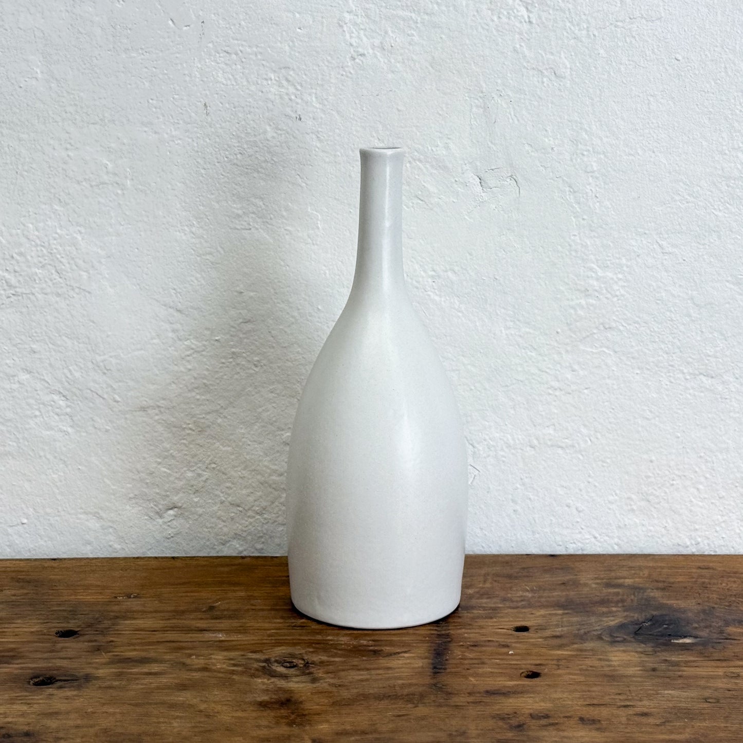 White ceramic vase on a wooden surface with a white textured wall background