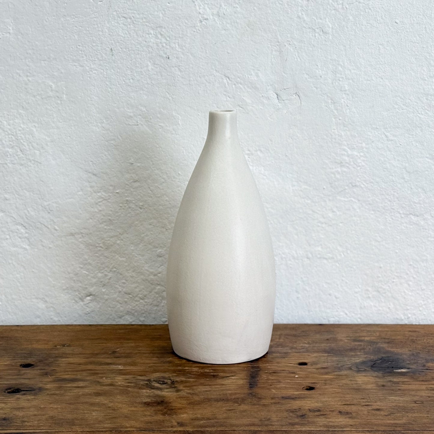 White ceramic vase on a wooden surface with a white textured wall background
