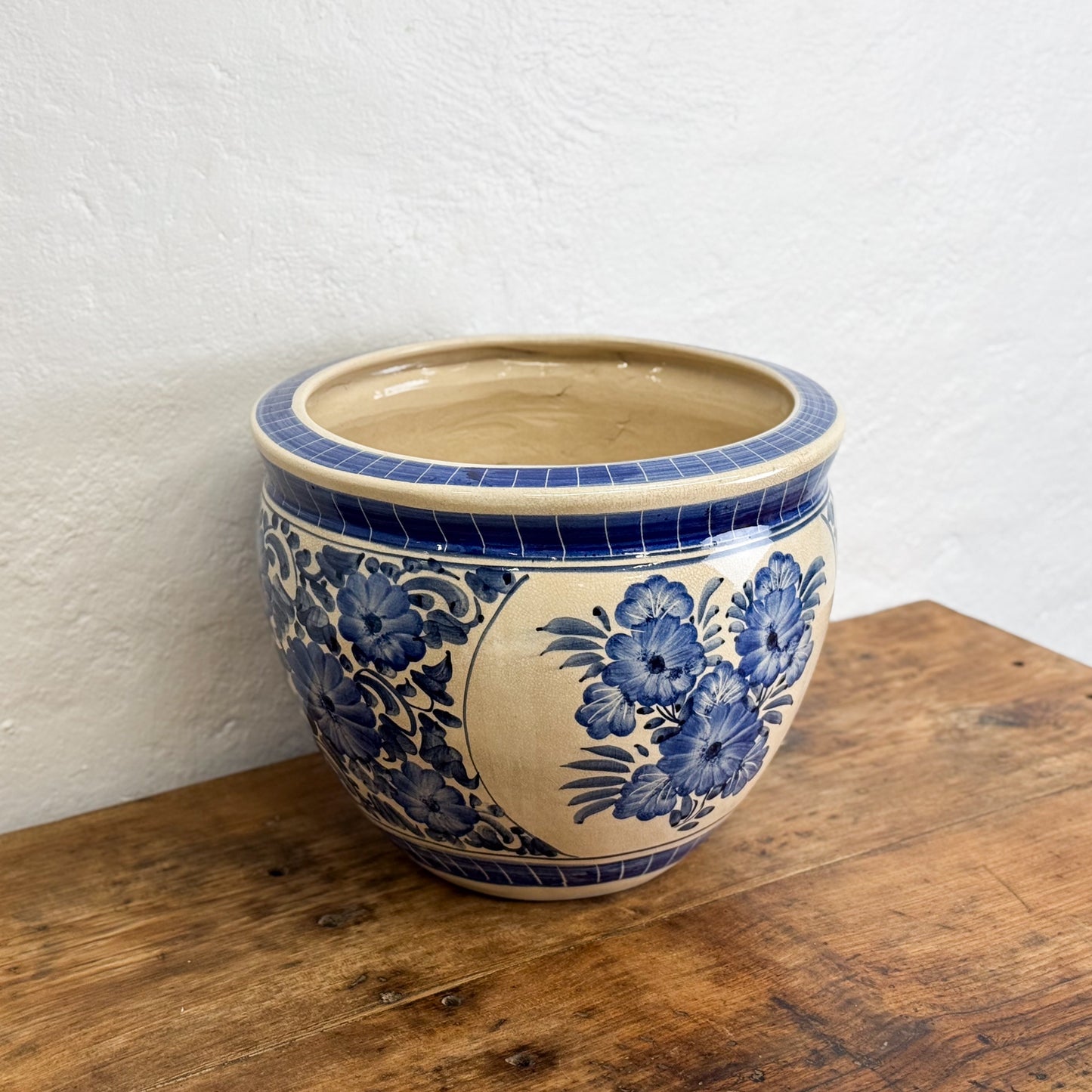 Ceramic pot with blue floral patterns on a wooden surface against a white wall