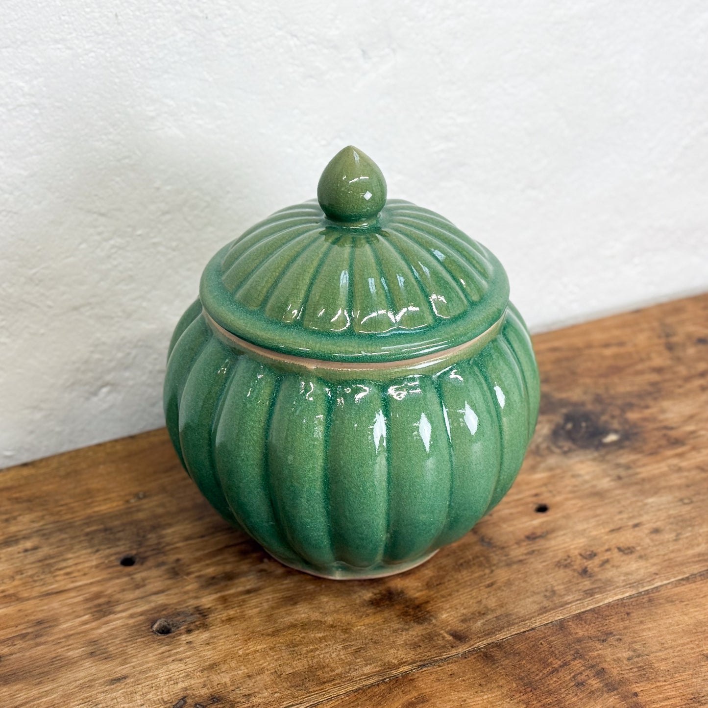 Green ceramic jar with a lid on a wooden surface