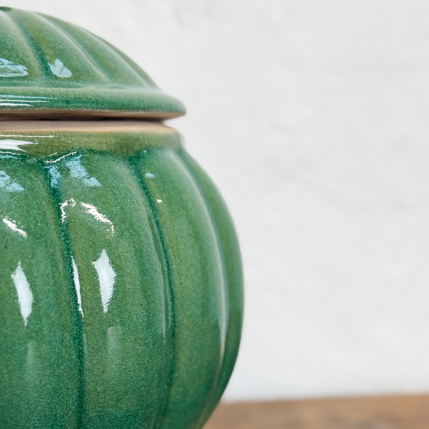 Green ceramic jar with lid on a wooden surface and white background