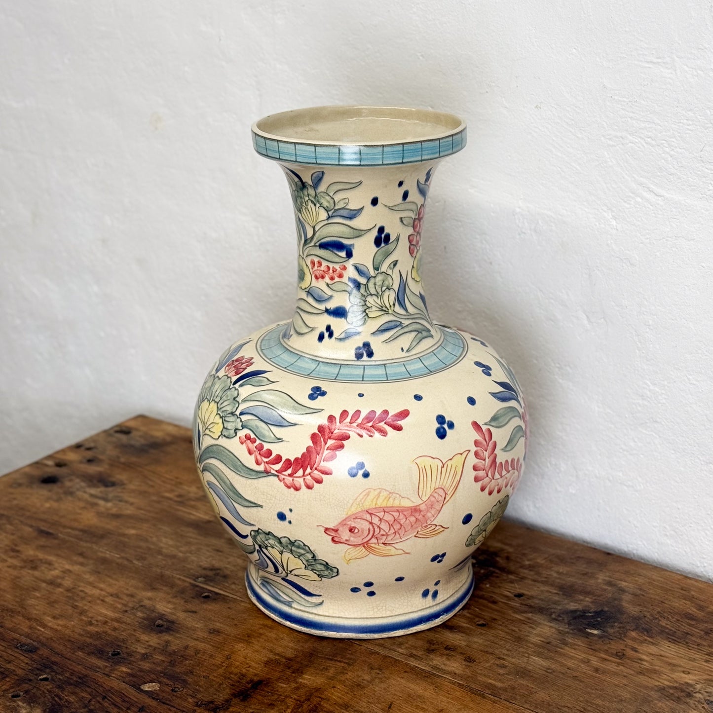 Decorative ceramic vase with floral and fish designs on a wooden surface.