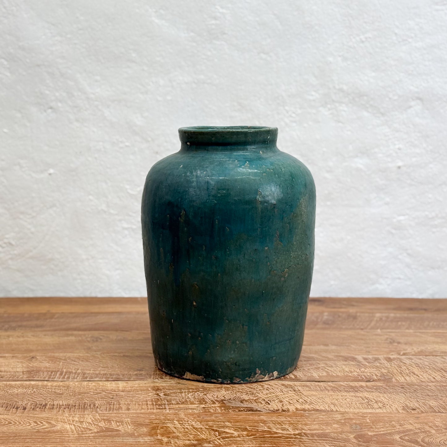 Green ceramic jar on a wooden surface with a textured white wall background