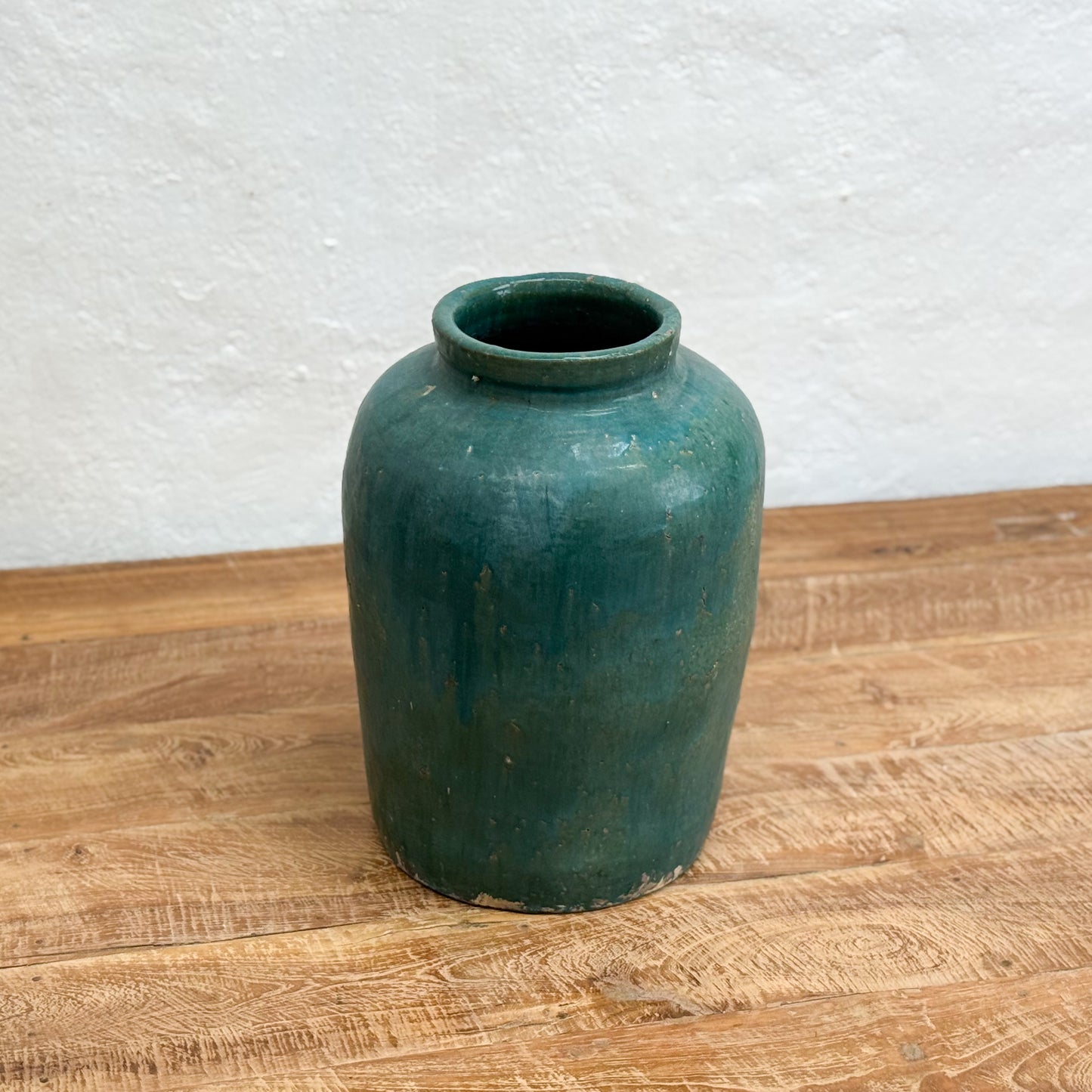 Green ceramic vase on a wooden surface with a white textured wall background