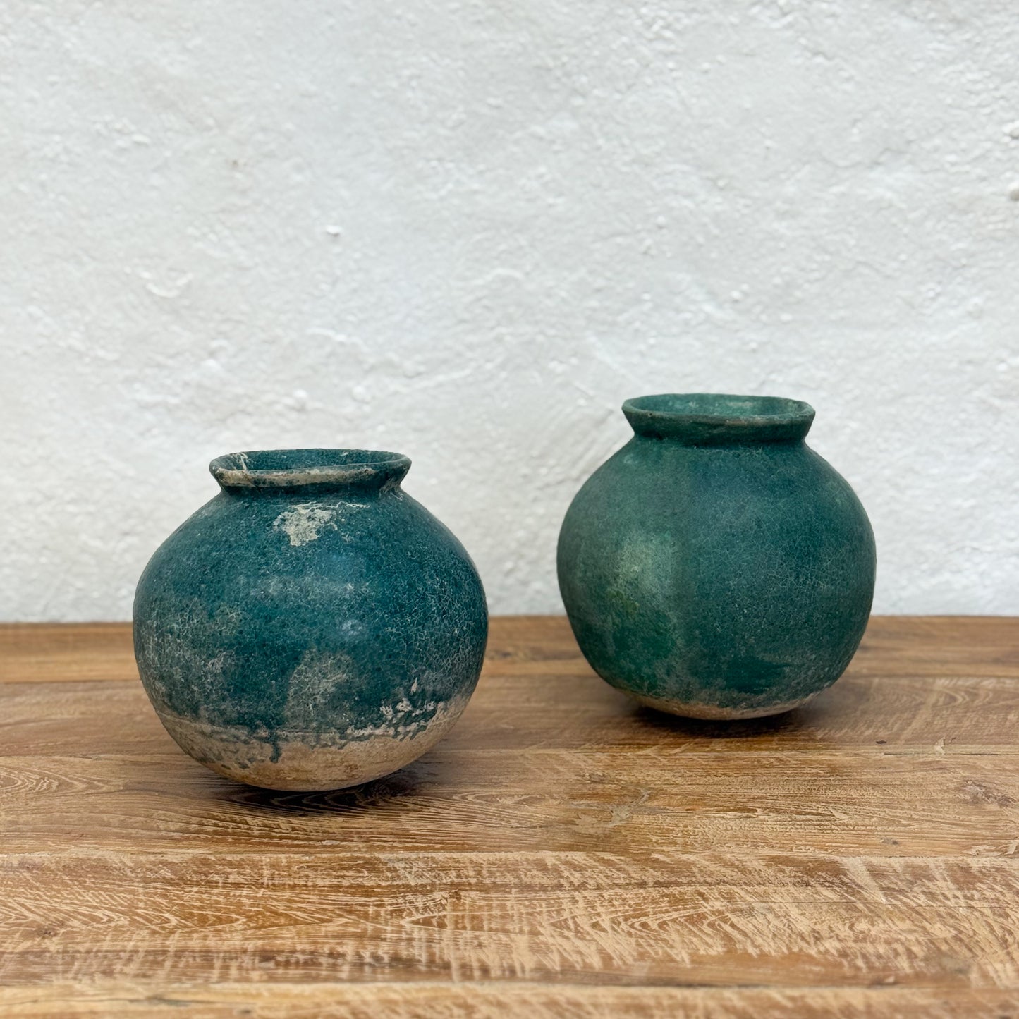 Two green ceramic pots on a wooden surface with a textured white wall background