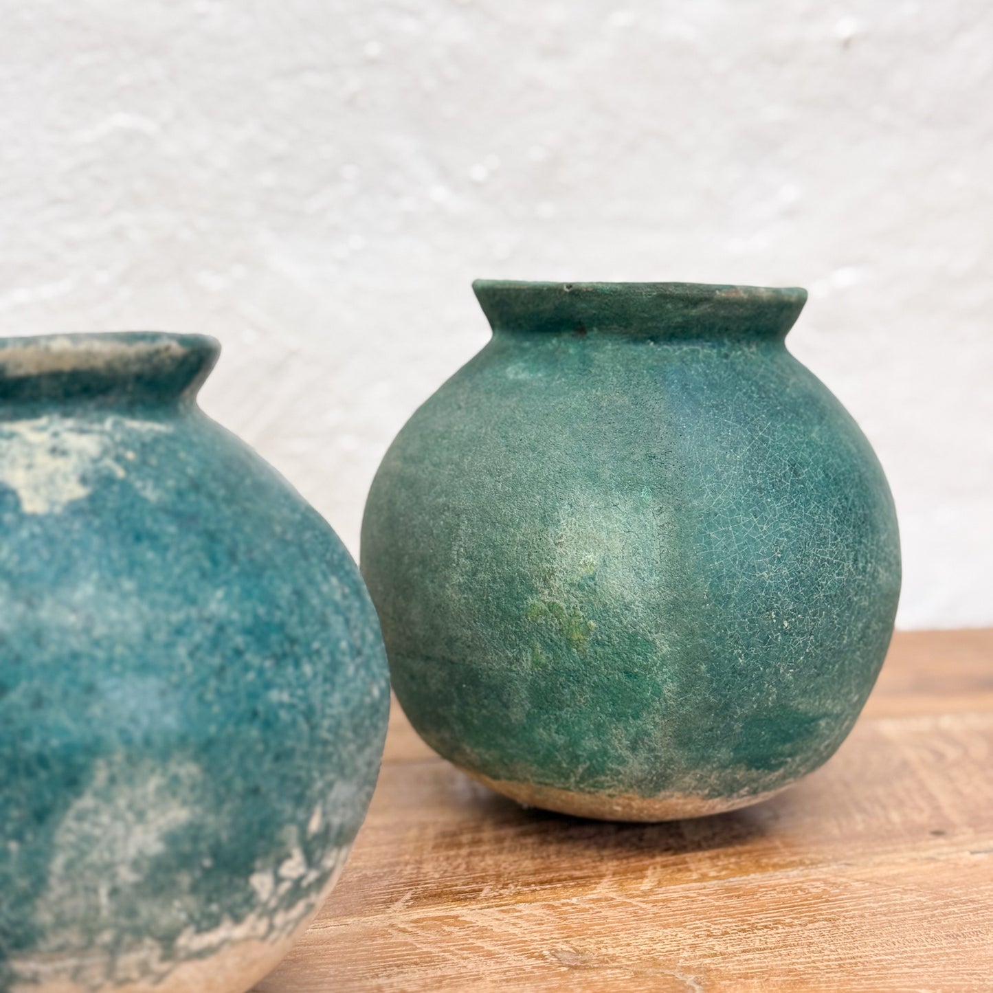 Two green ceramic pots on a wooden surface with a light gray background