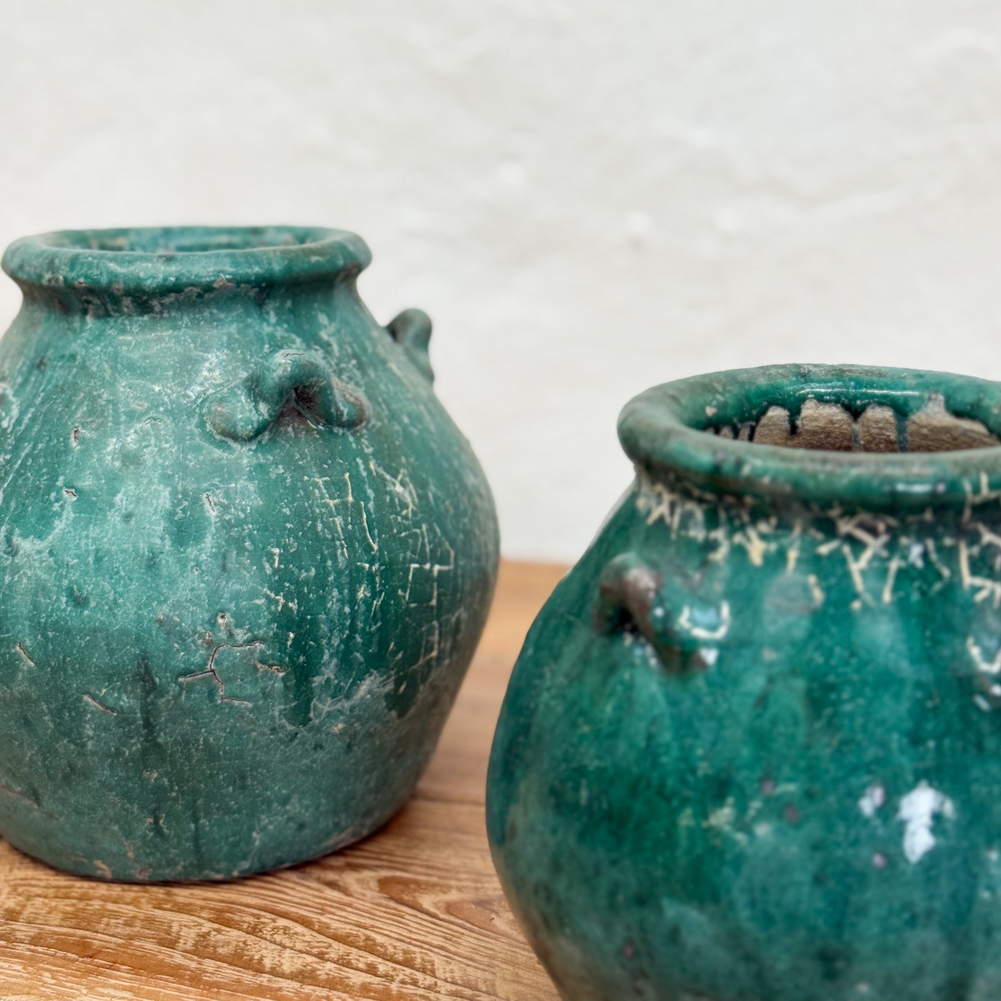 Two green ceramic pots on a wooden surface with a white background