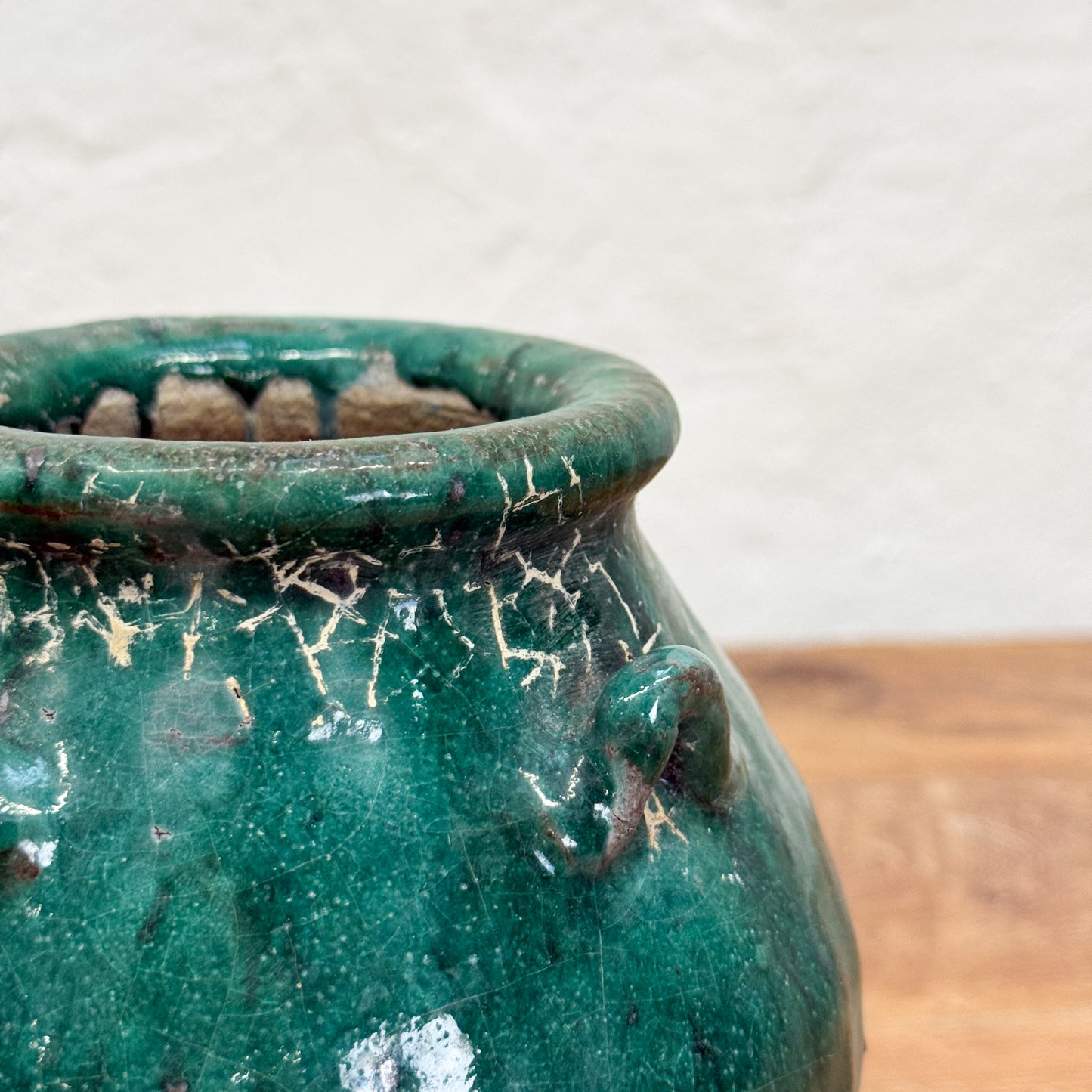 Green ceramic pot with a textured surface on a wooden surface.