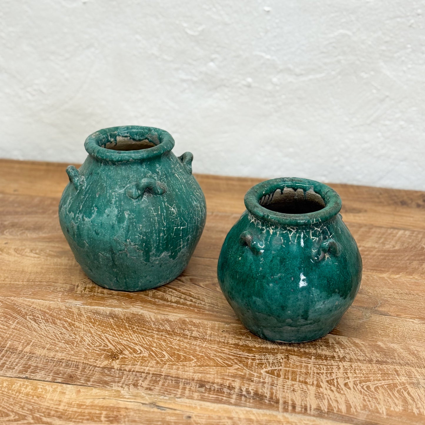 Two green ceramic pots on a wooden surface with a white textured wall background.
