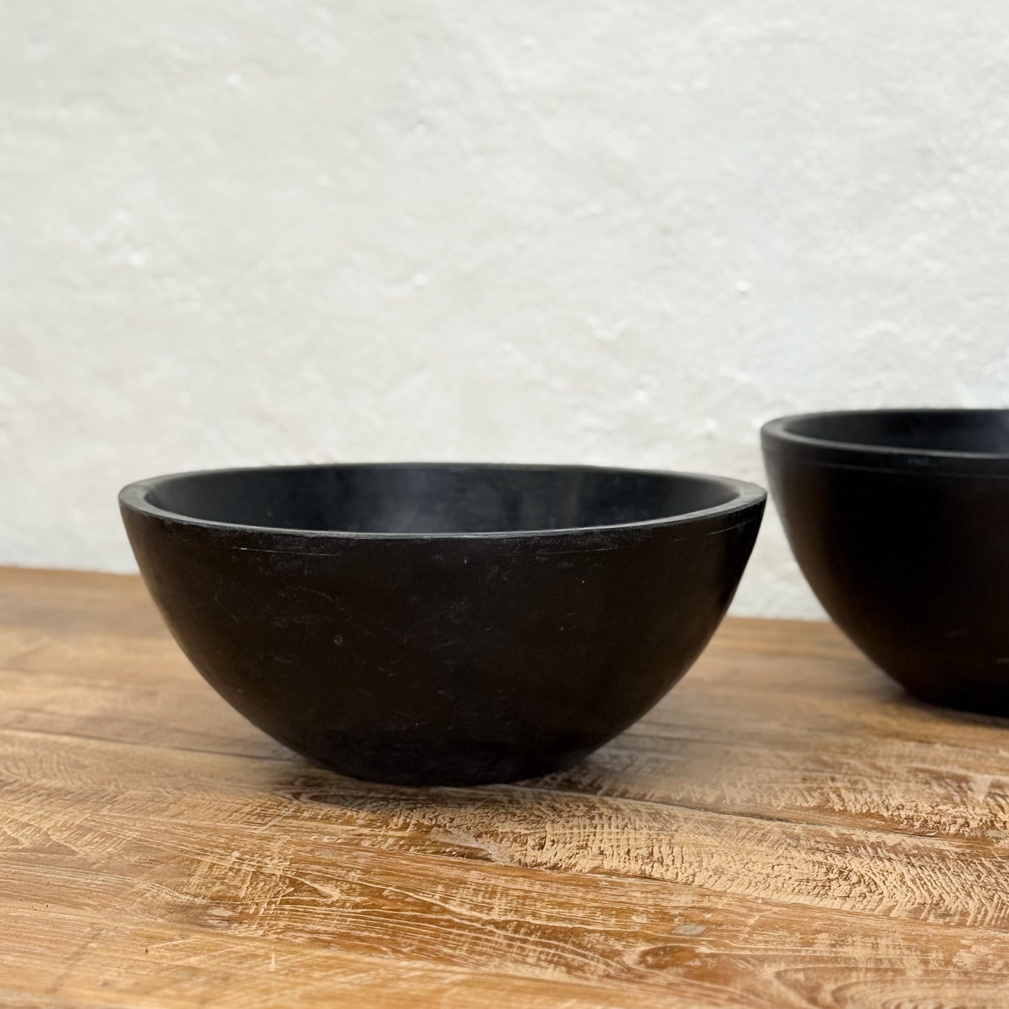 Two black bowls on a wooden surface with a light gray textured wall in the background.