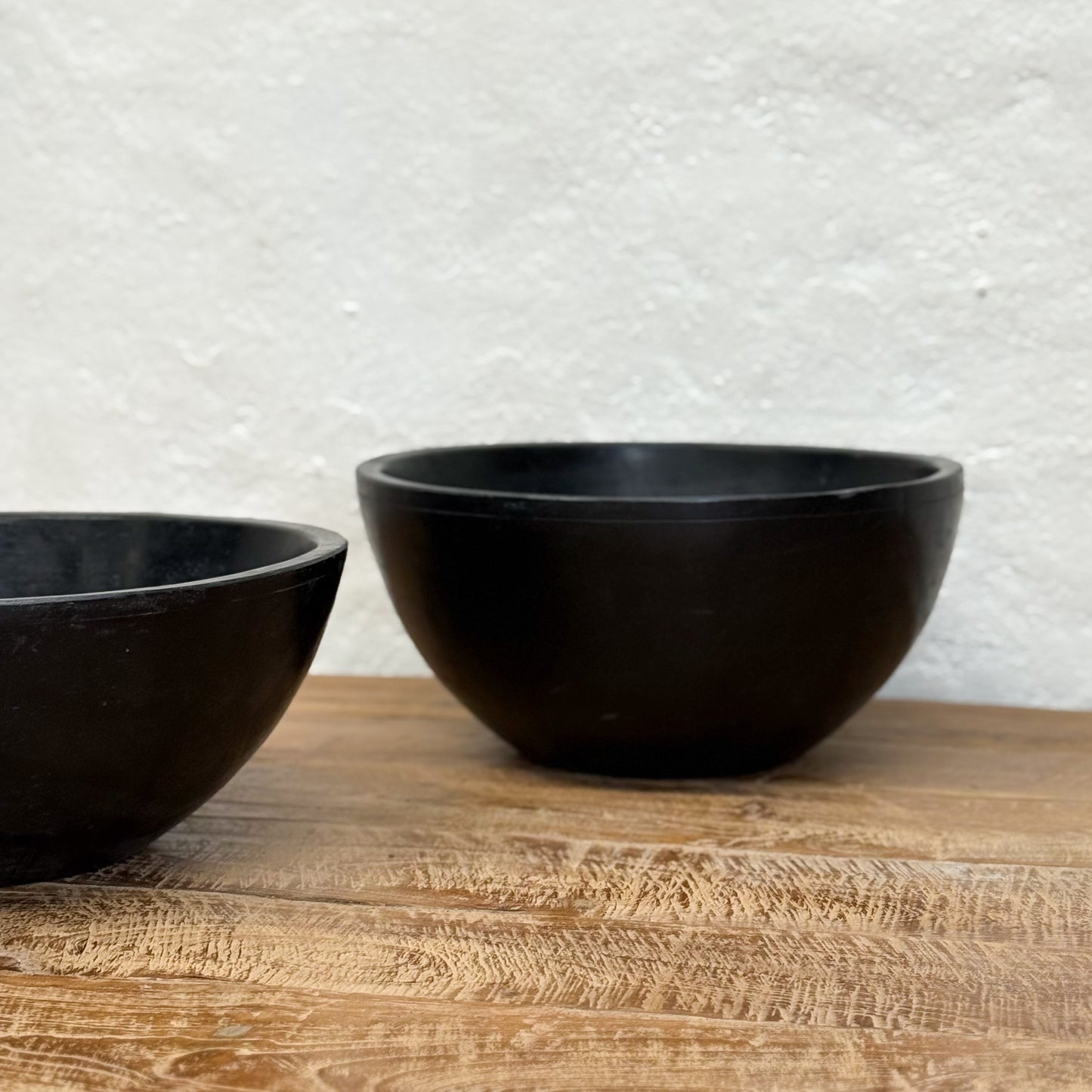 Two black bowls on a wooden surface with a textured white wall background