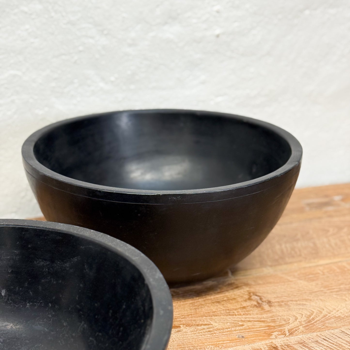 Two black bowls on a wooden surface with a light gray textured background