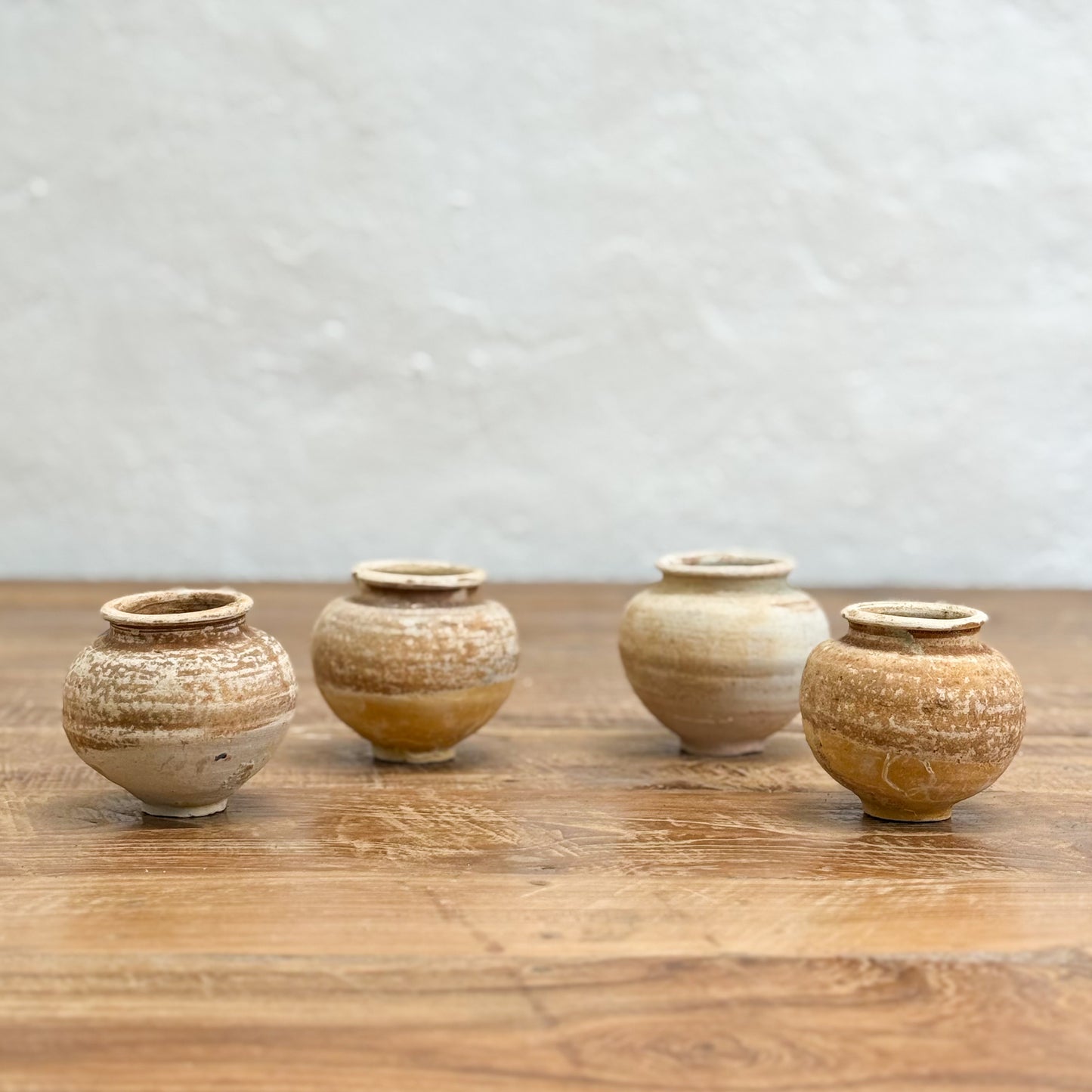 Four small ceramic pots on a wooden surface with a light gray textured background
