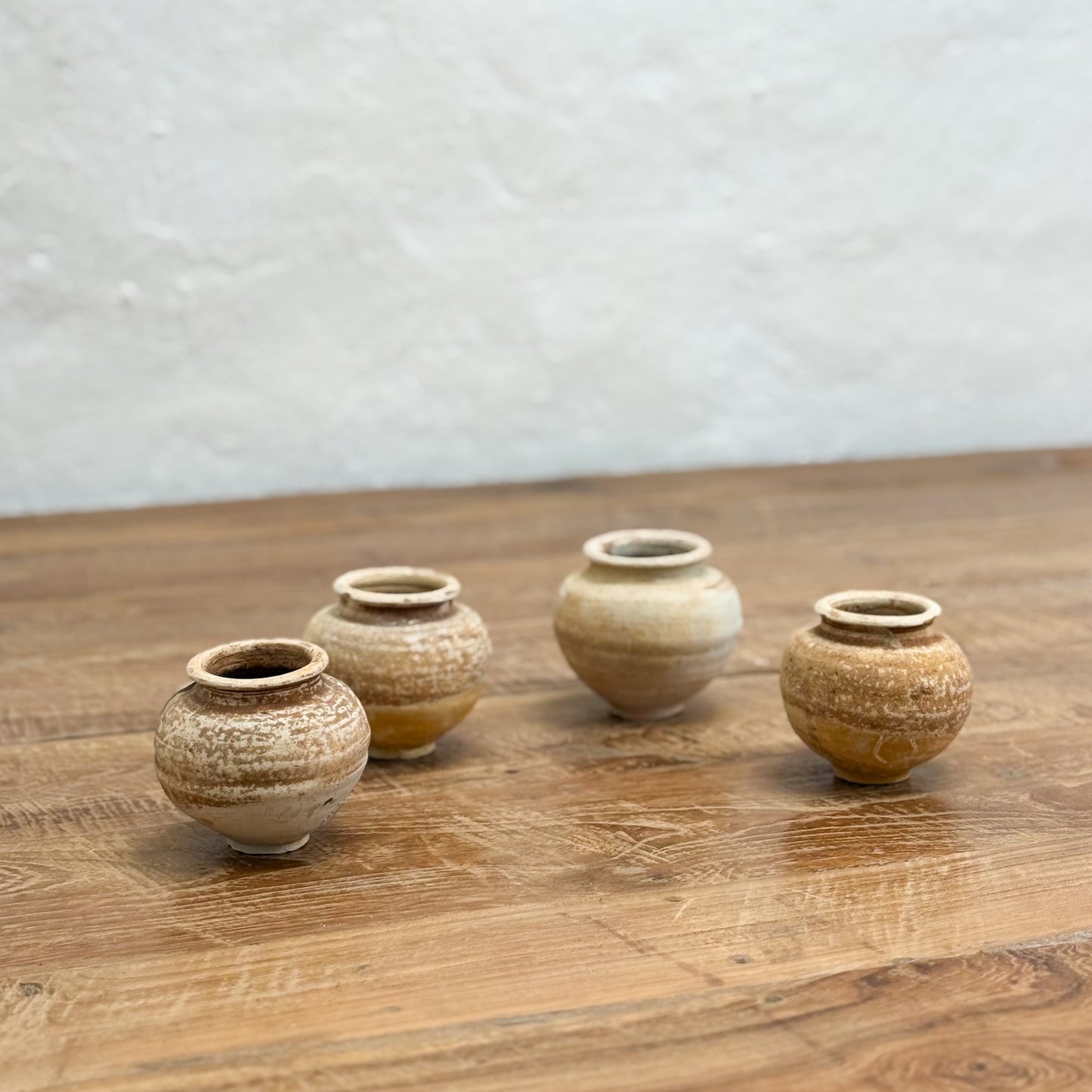 Four small ceramic pots on a wooden surface with a light gray background