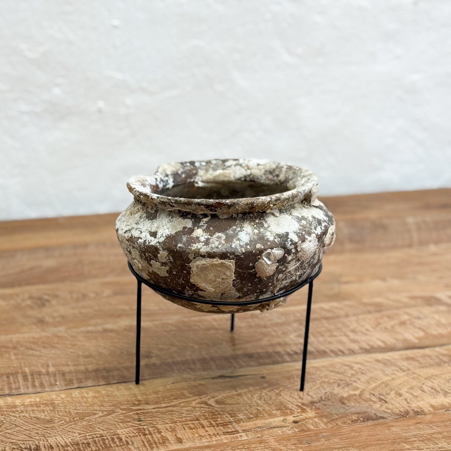 Vintage-style pot on metal stand on a wooden surface with a white wall background