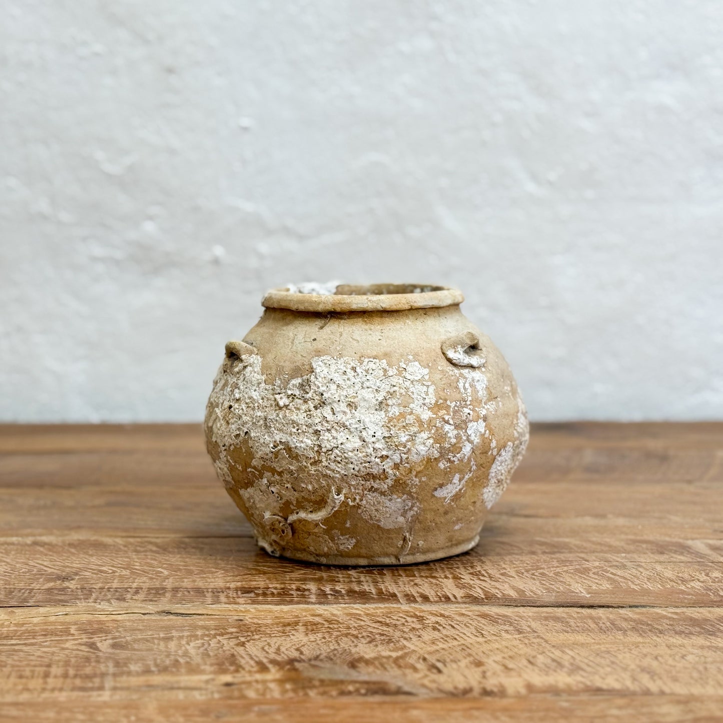 Vintage ceramic pot on a wooden surface with a textured gray wall background