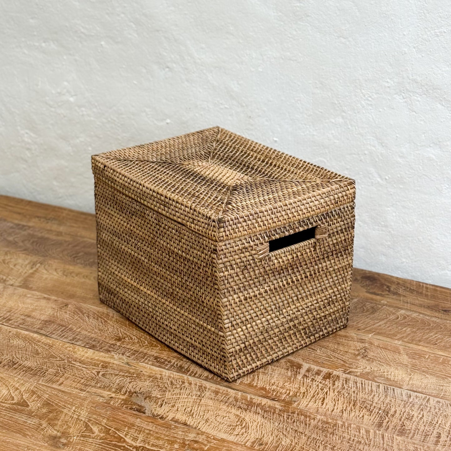 Woven storage basket on a wooden surface with a white textured wall background