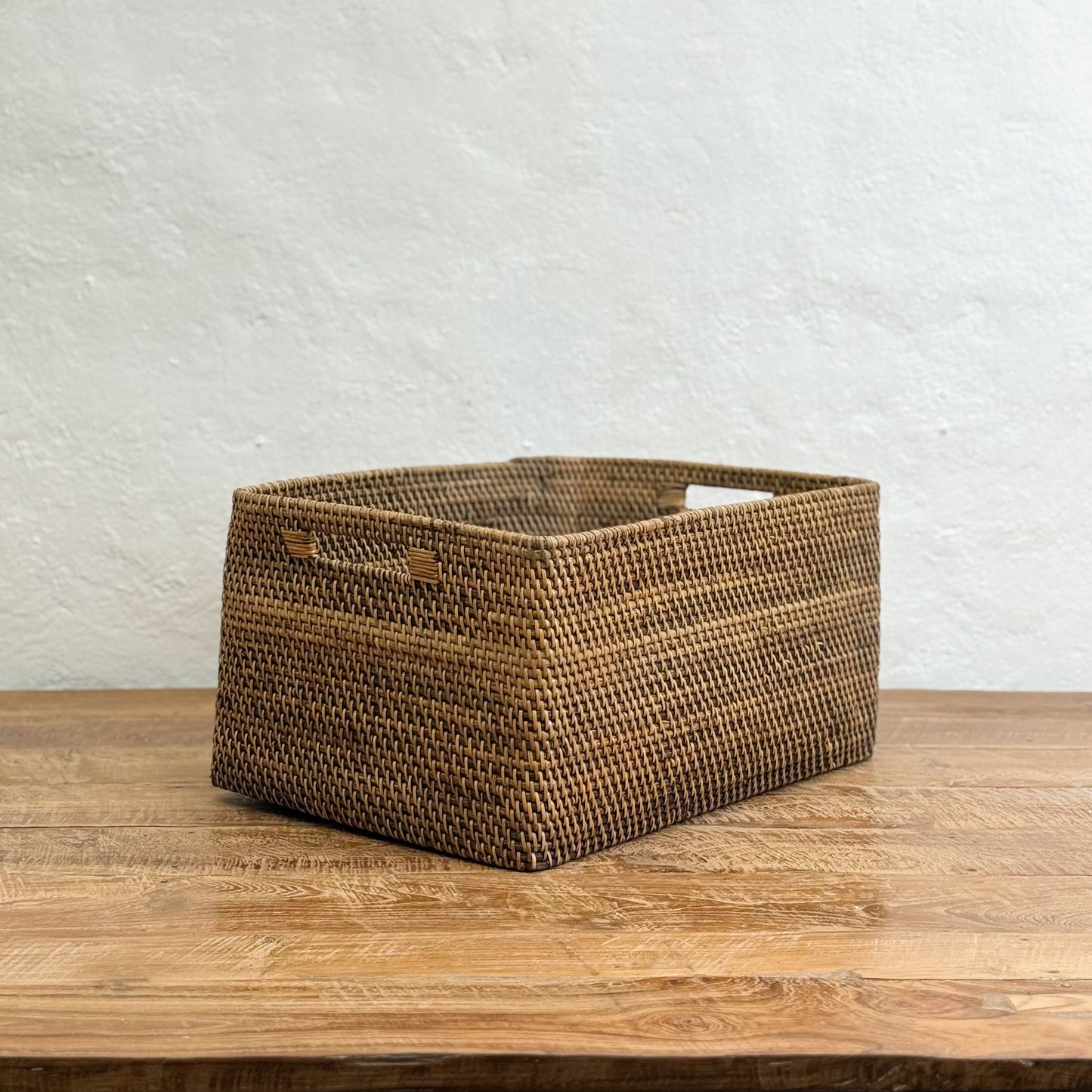 Woven brown basket on a wooden surface with a light gray textured wall background