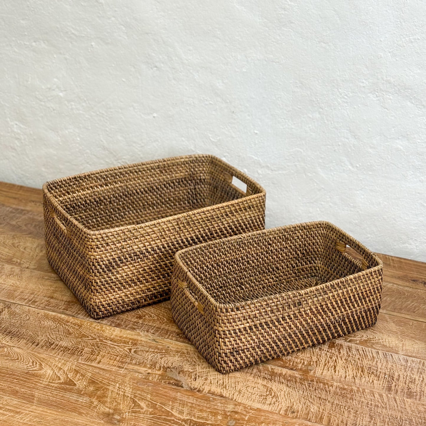 Two woven baskets on a wooden surface with a white textured wall background