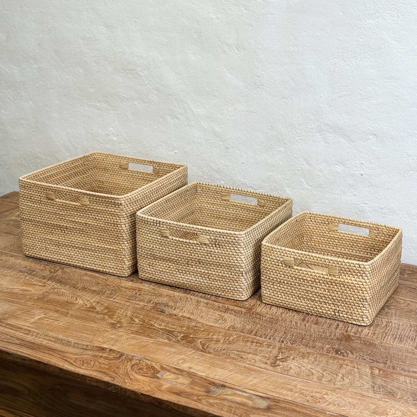 Three woven baskets of different sizes on a wooden surface with a light gray background
