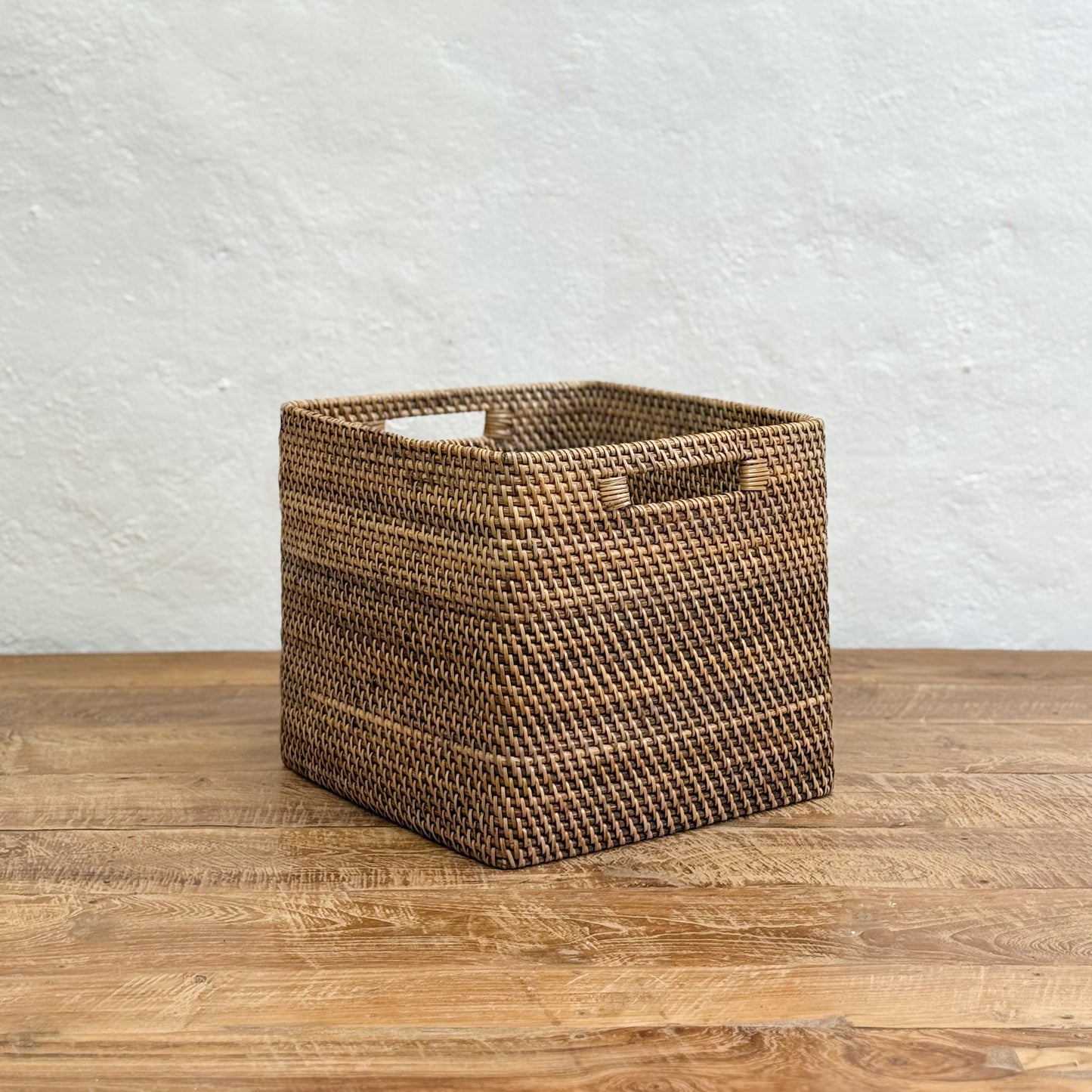 Woven brown basket on a wooden surface with a light gray textured wall background