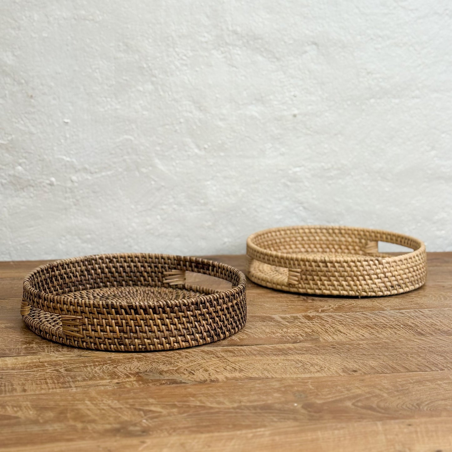 Two woven baskets on a wooden surface with a light gray textured wall background