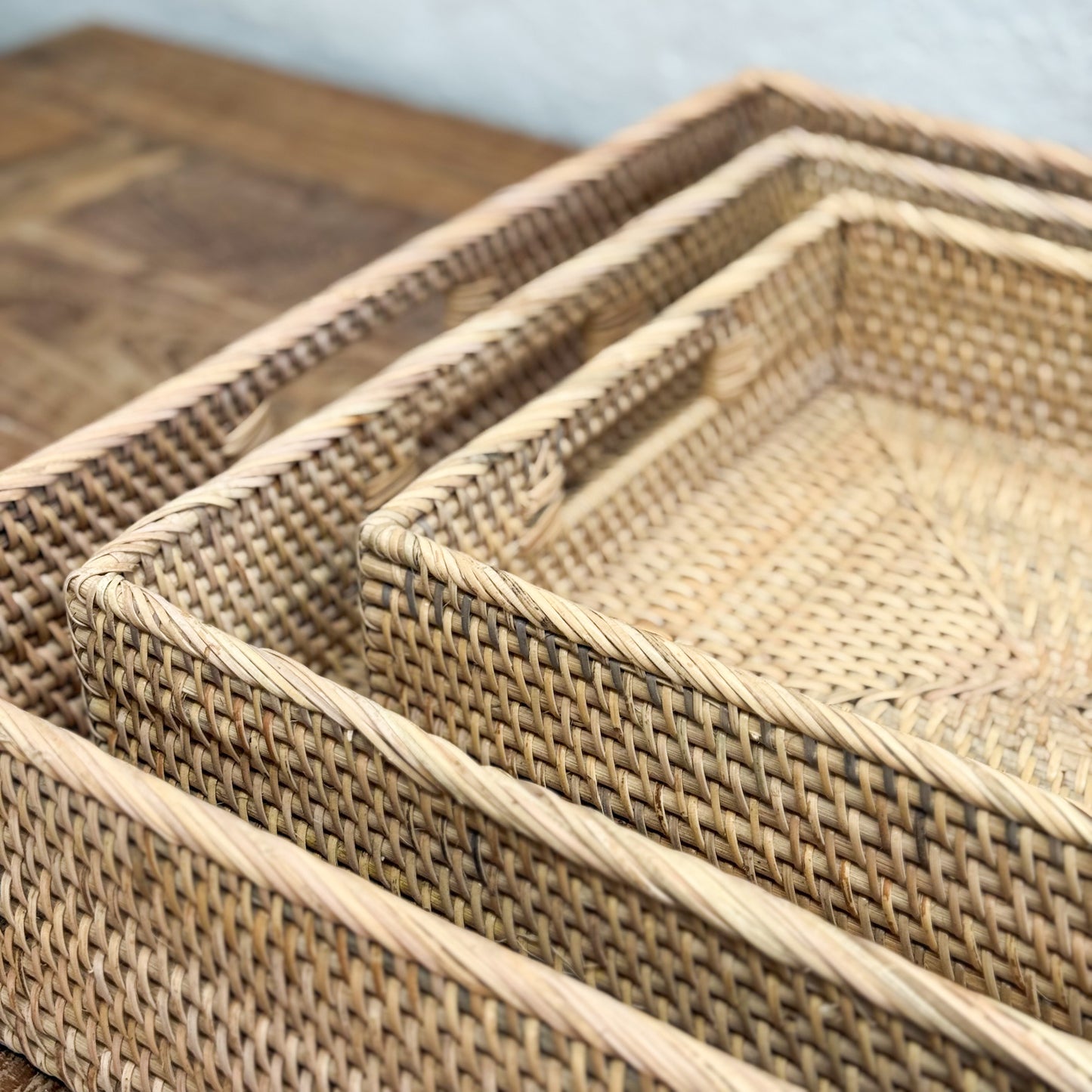 Set of woven rattan trays on a wooden surface with a light blue background
