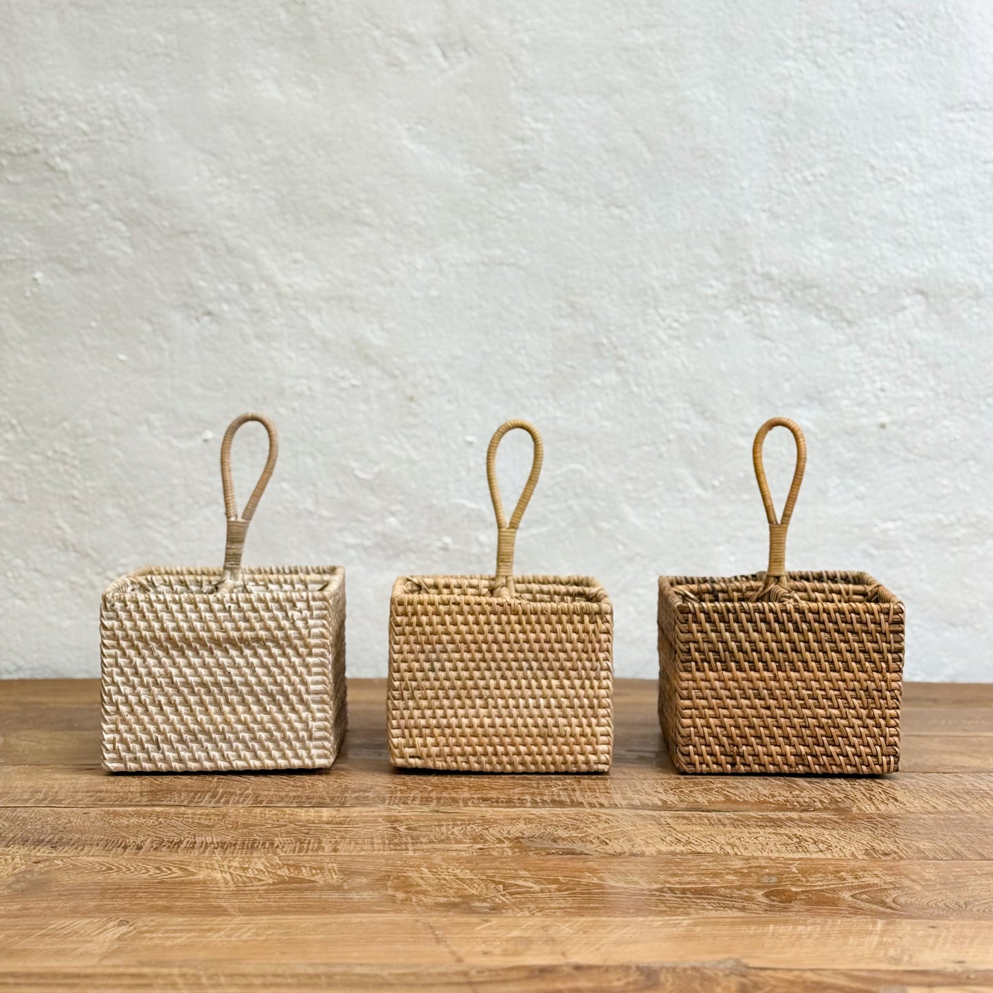 Three woven baskets with handles on a wooden surface and light gray background