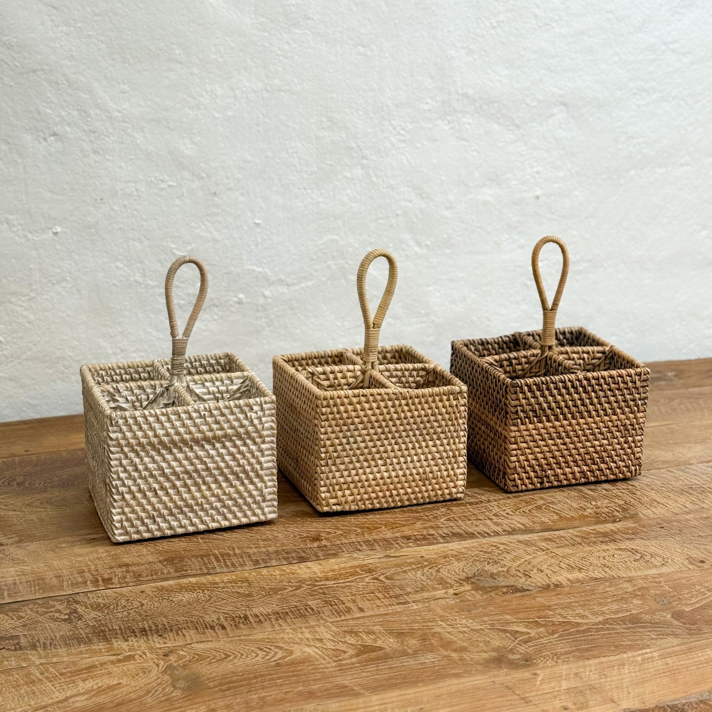 Three woven baskets with handles on a wooden surface against a light wall.