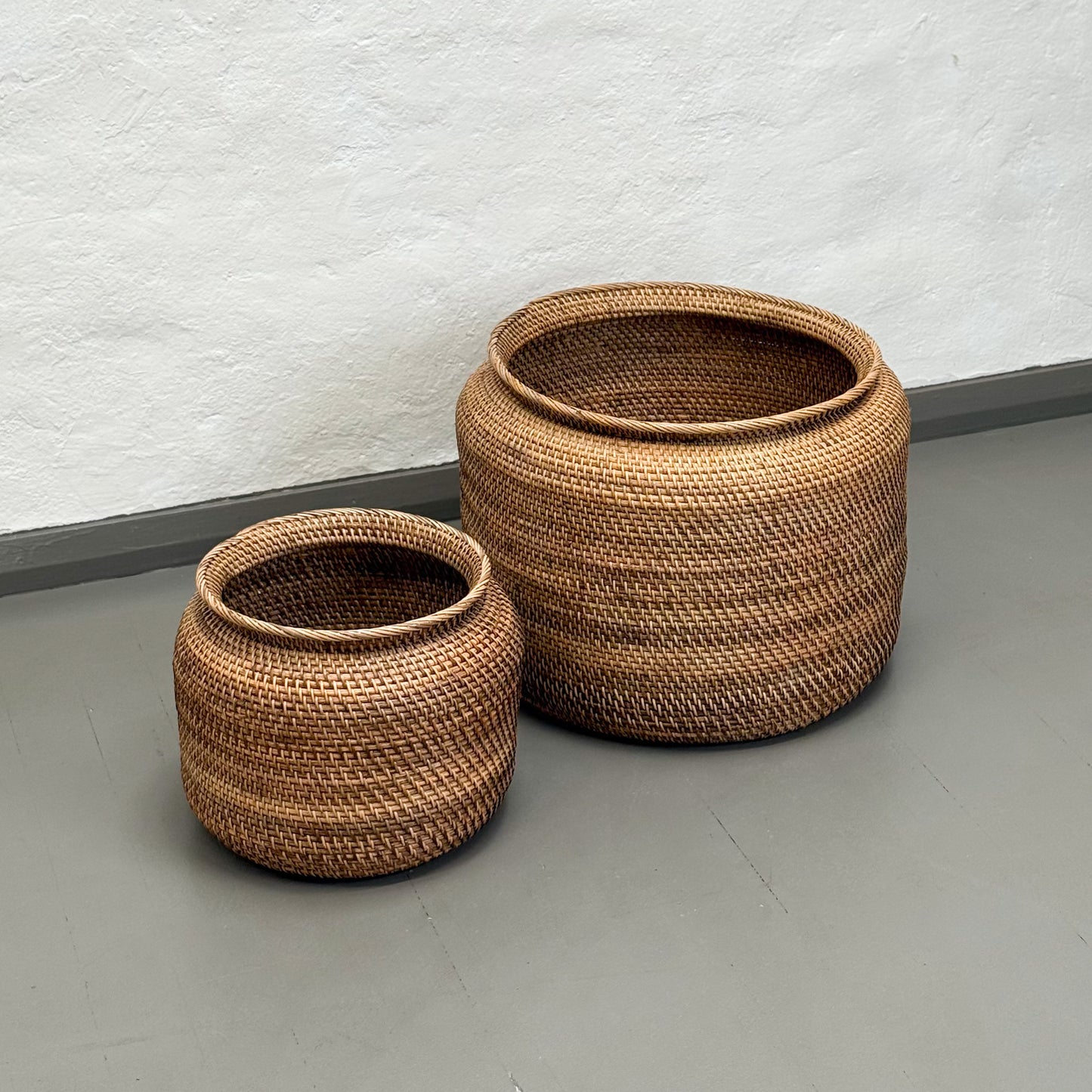 Two woven baskets on a plain floor with a white wall background
