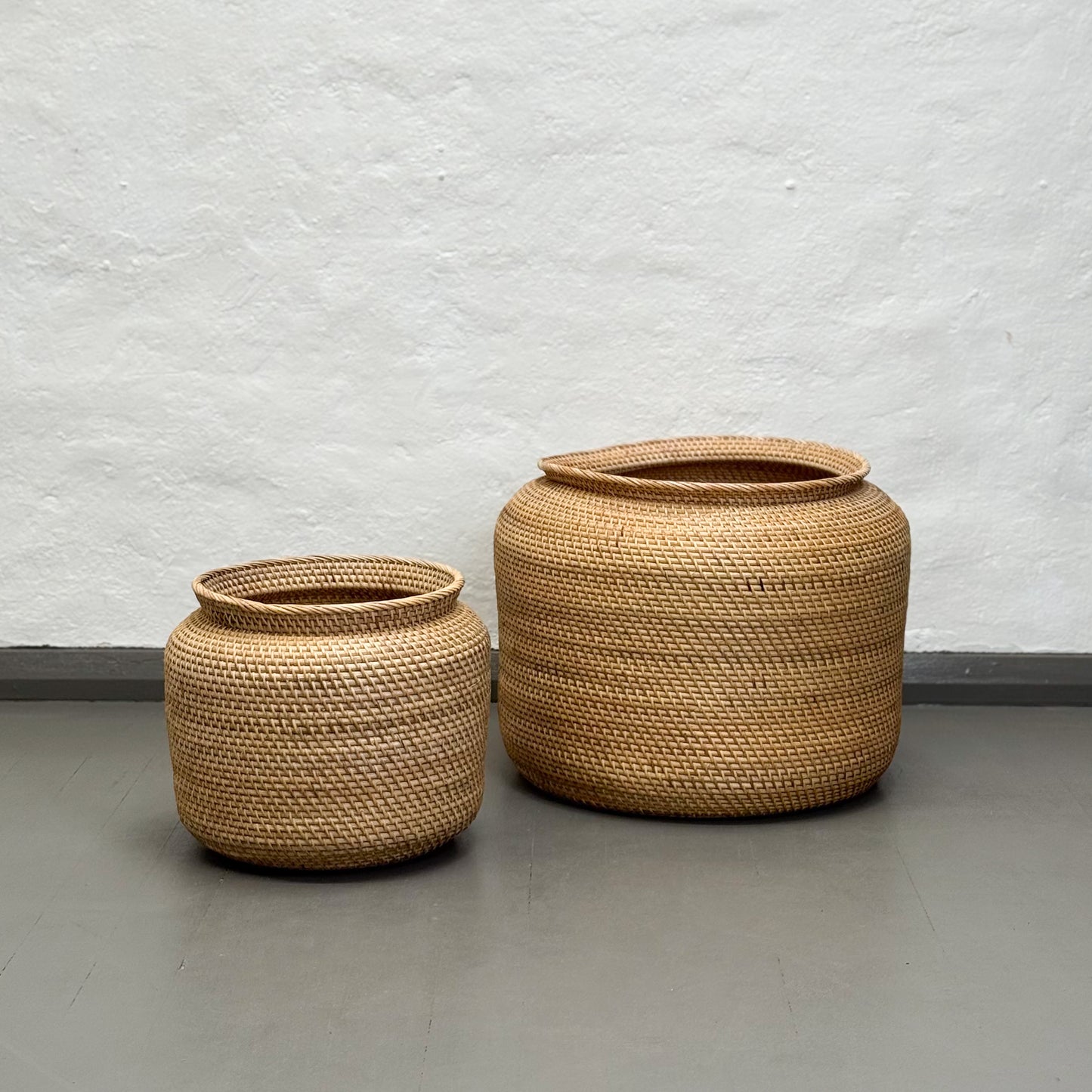 Two woven baskets on a plain floor with a light gray wall background